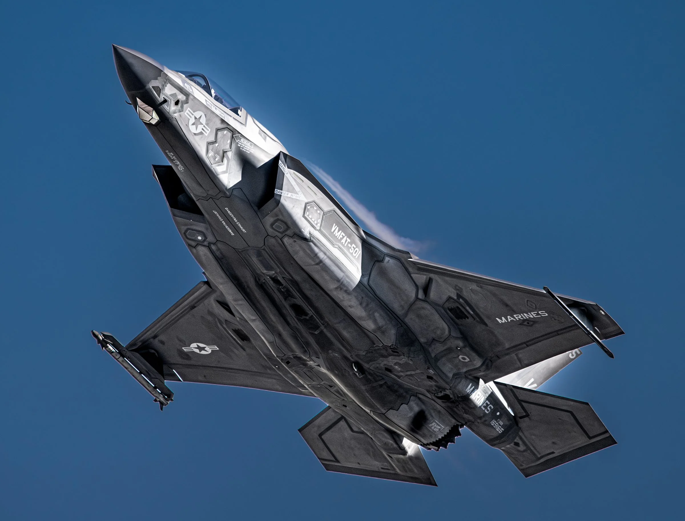 A black F-35 fighter jet flying in clear blue sky.