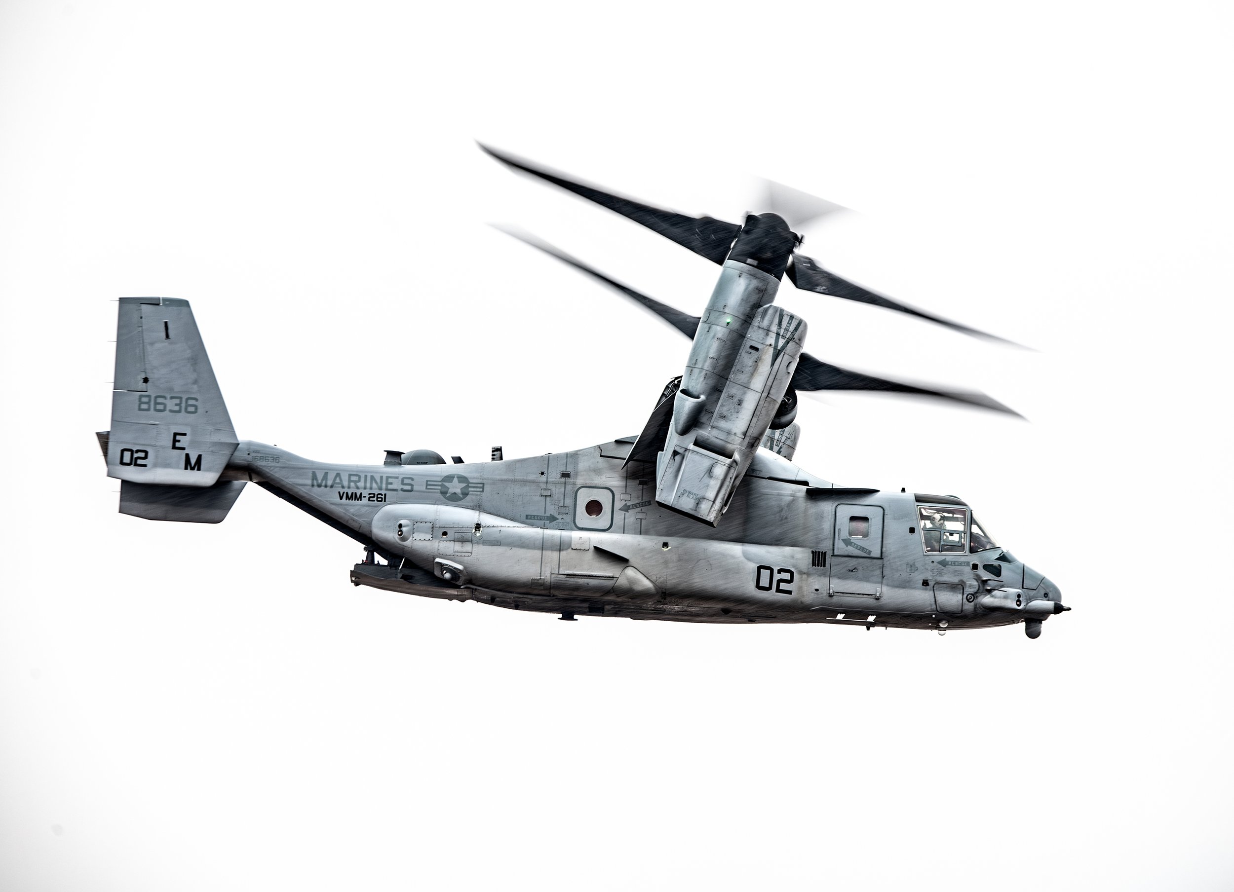 A gray military helicopter in flight against a white background.
