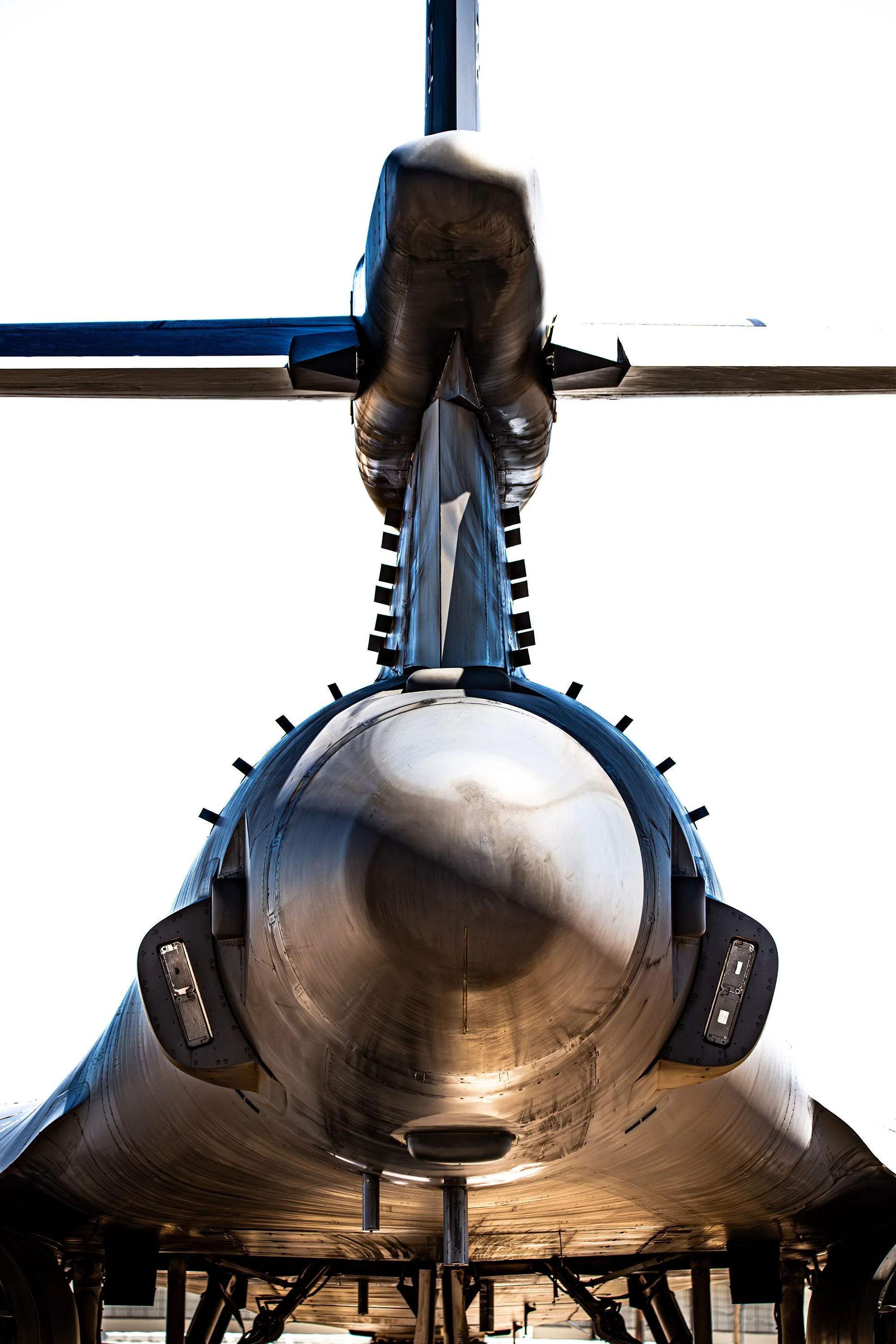 Front view of a fighter jet aircraft from below, showing its nose and cockpit, with the sky in the background.