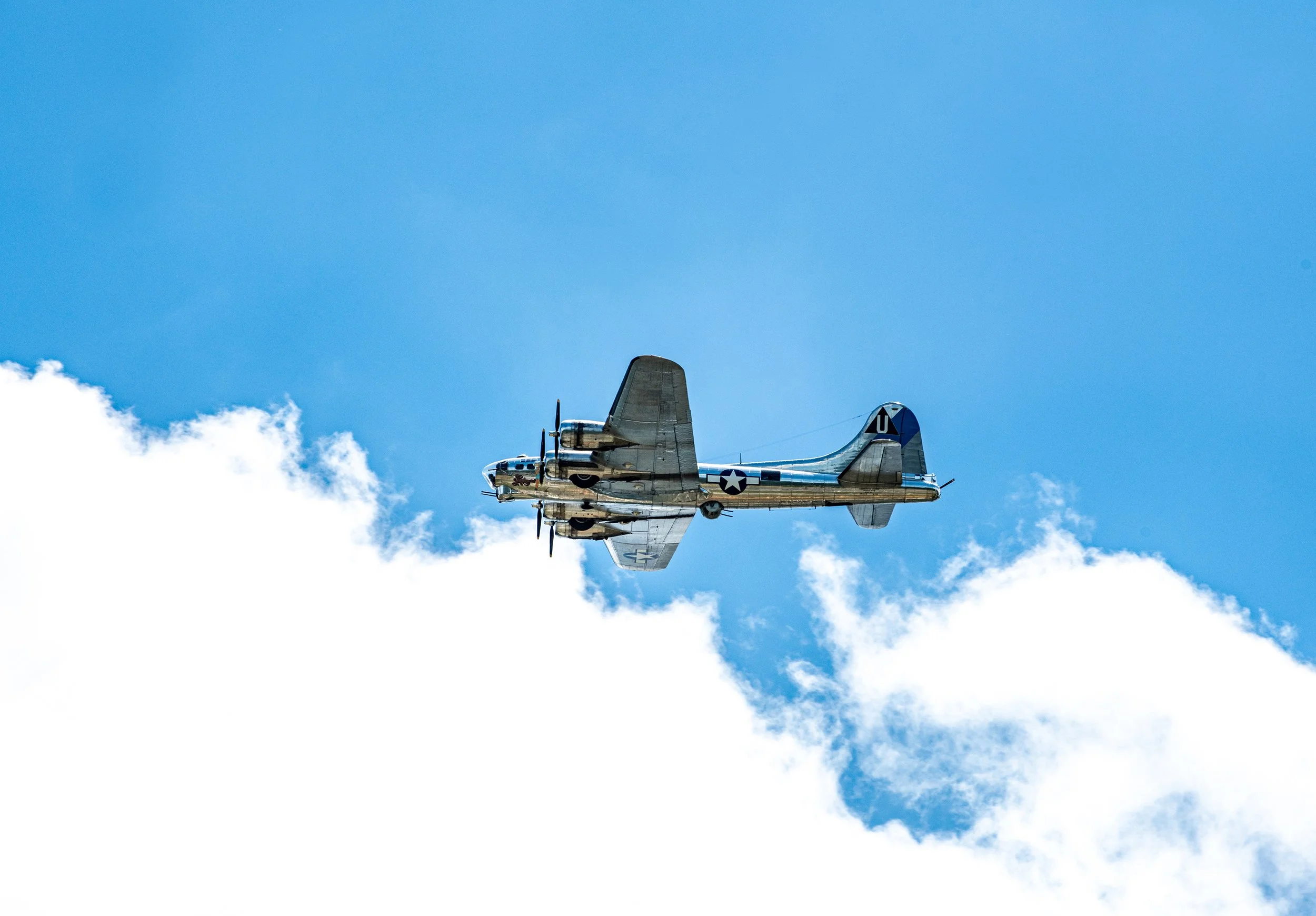 A vintage military aircraft flying in the sky with some clouds below.