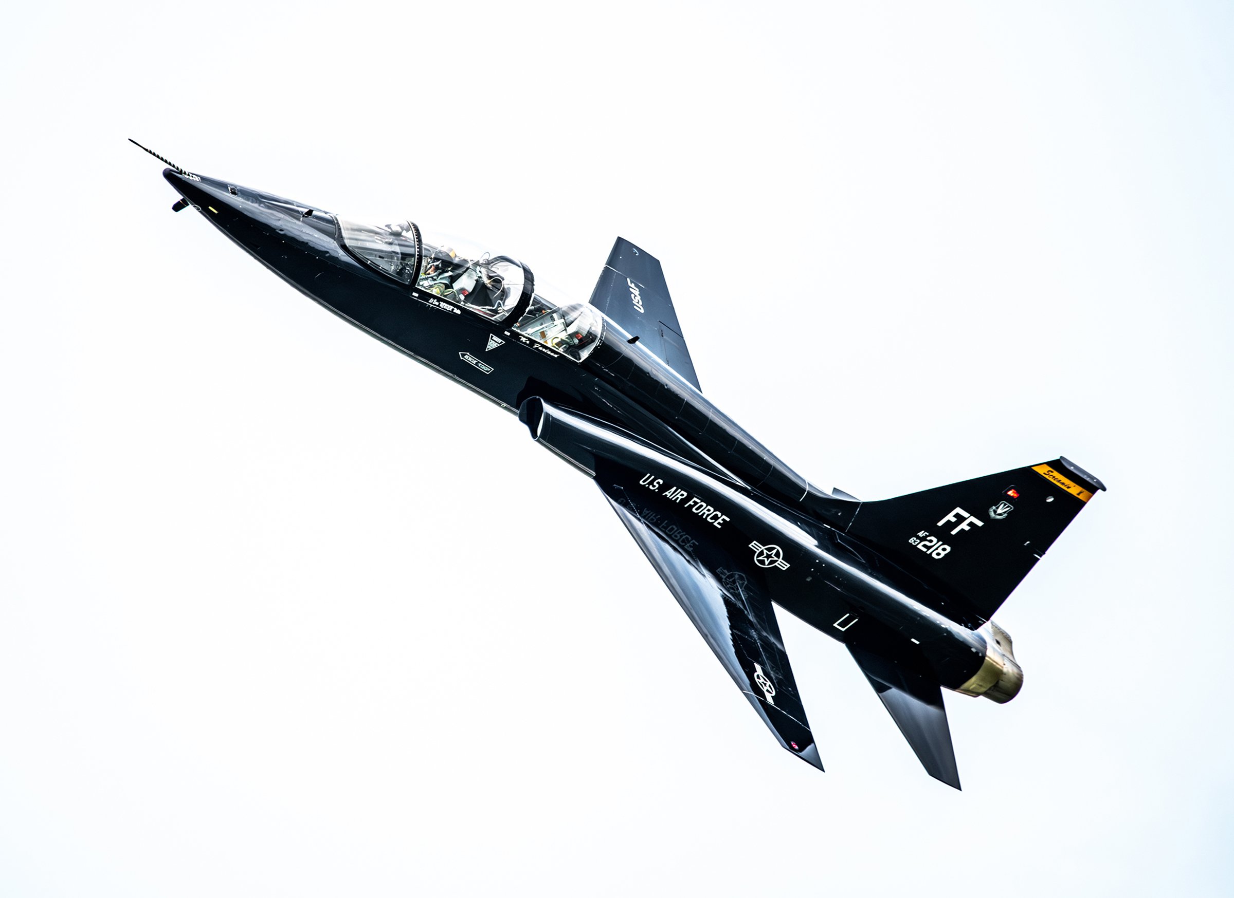 A black U.S. Air Force fighter jet flying through the sky at an angle.