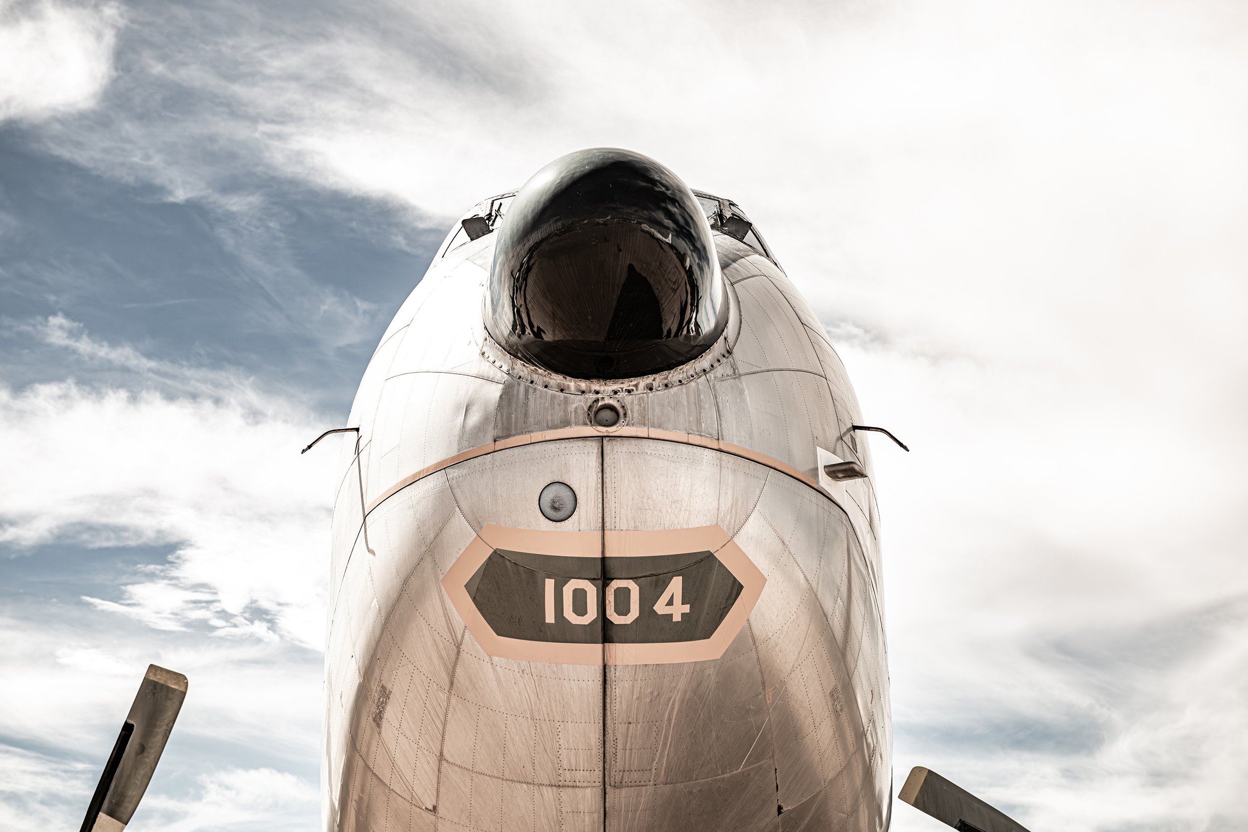 Front view of a military aircraft with the number 1004 on its nose, set against a cloudy sky.