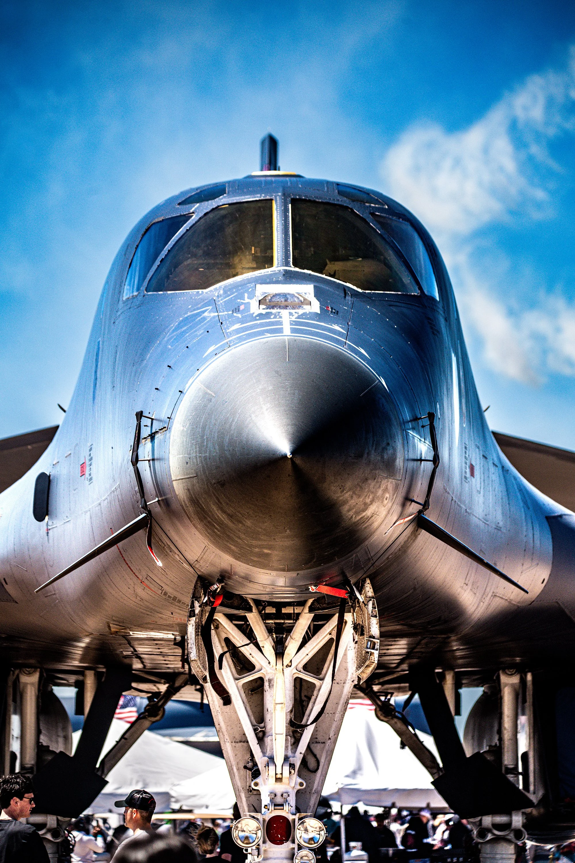 Front view of a military fighter jet on display at an airshow, with people observing underneath.