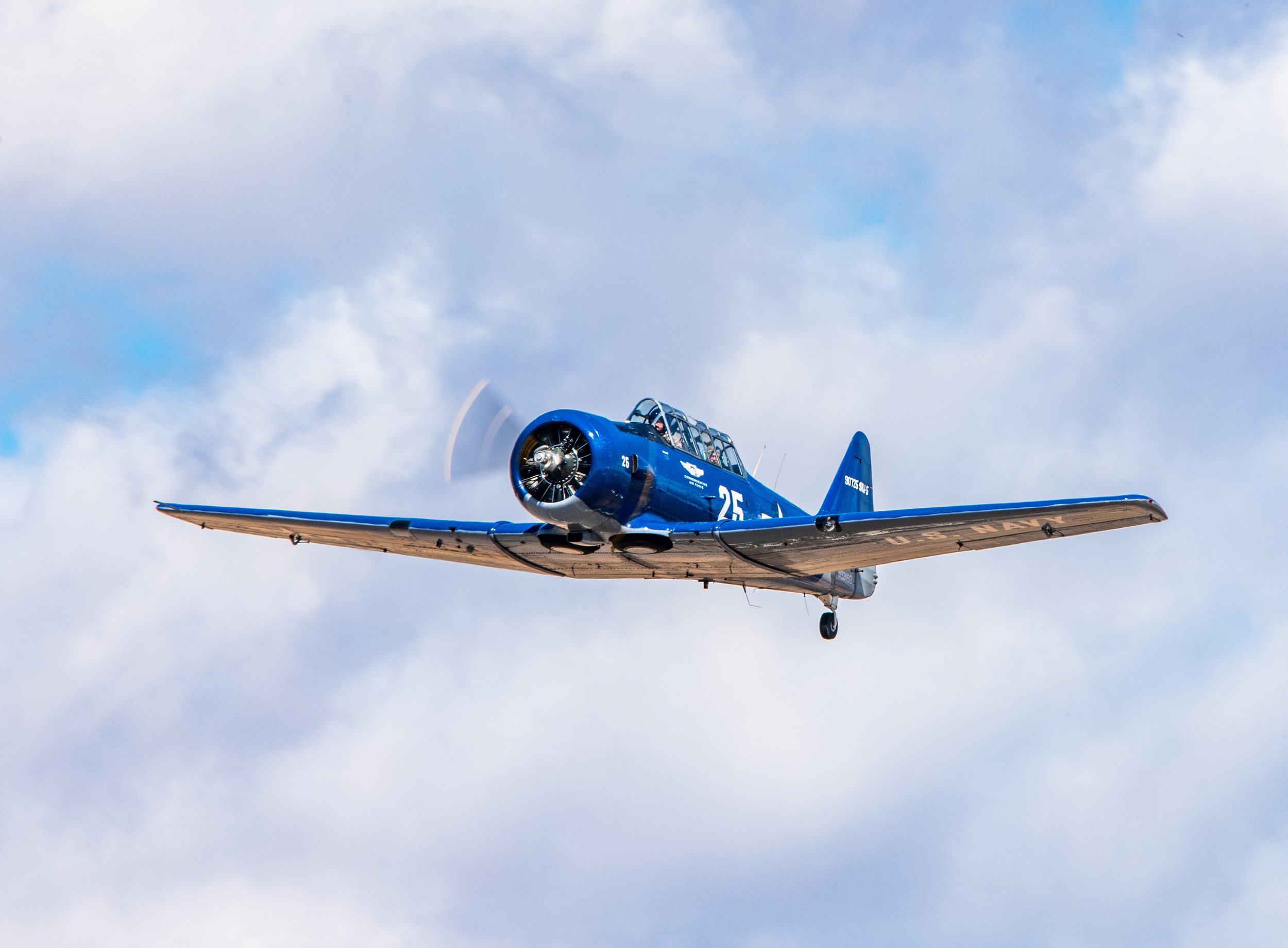 Blue vintage aircraft flying in the sky with clouds in the background.