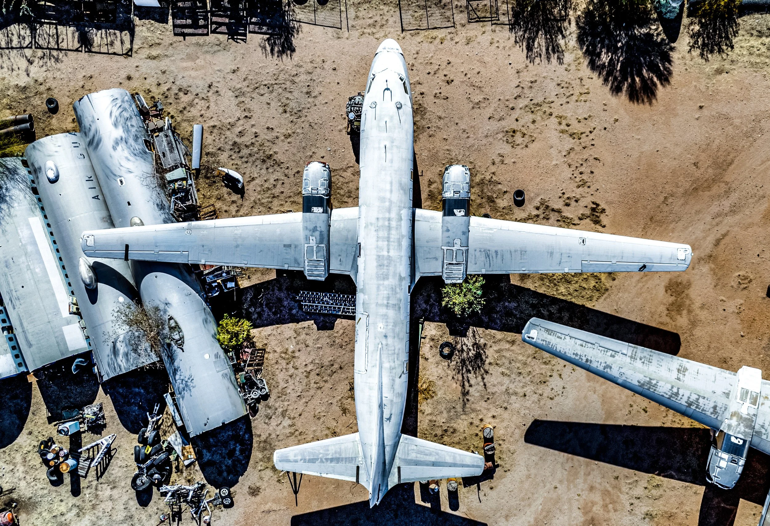 Aerial view of a large airplane parked on an open dirt area with several vintage aircraft and equipment nearby, casting long shadows.