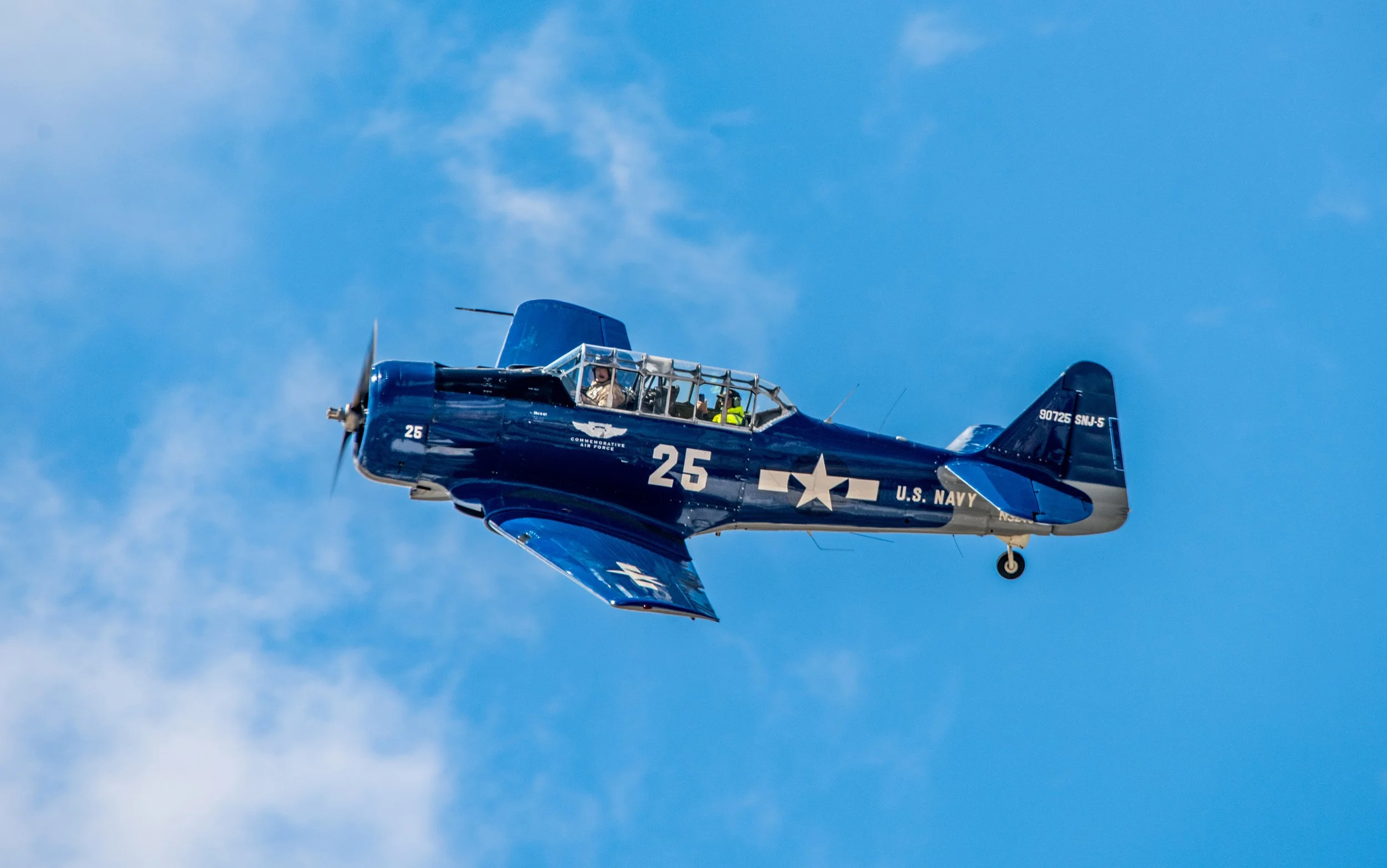 A vintage U.S. Navy blue aircraft flying in a clear blue sky.