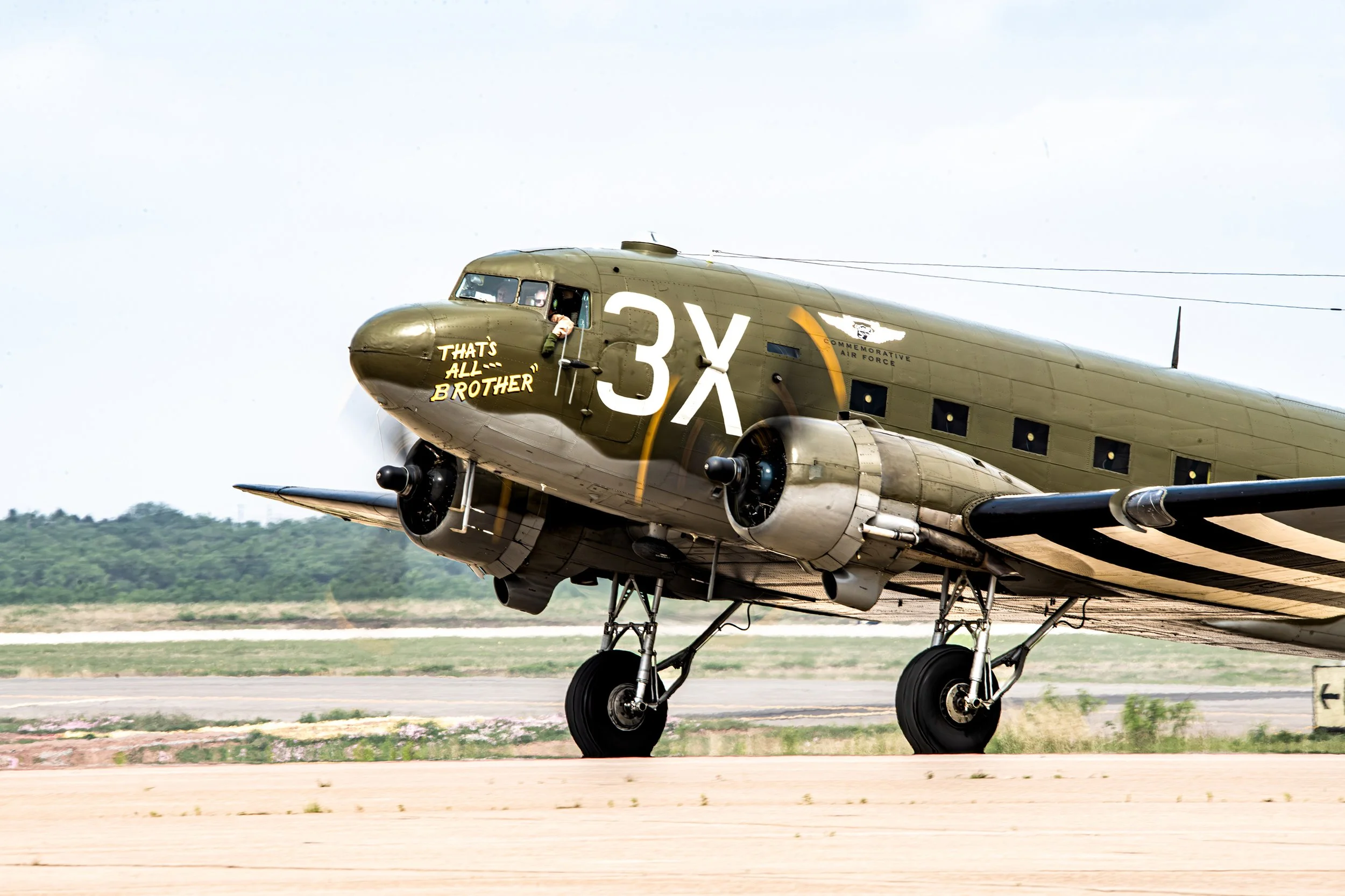 A vintage military airplane on the runway with military markings and the words 'That's all, brother' painted on the nose.