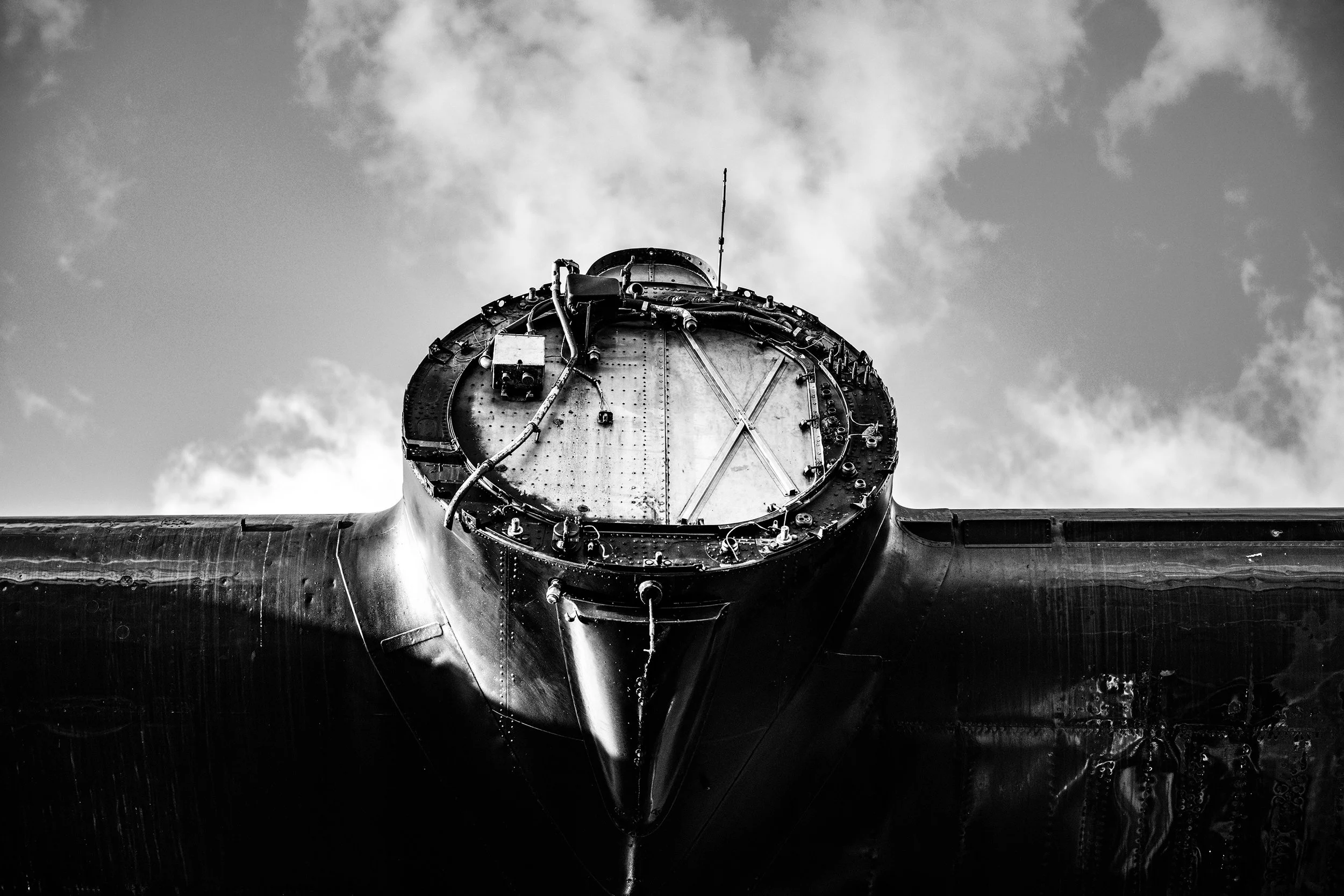 Black and white photo of an aircraft nose, viewed from below, with a cloudy sky in the background.