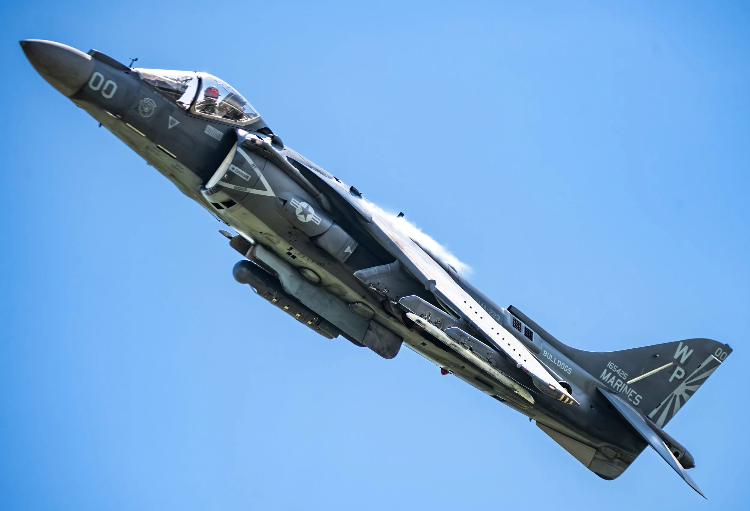 A fighter jet flying in a clear blue sky, with markings indicating it is a U.S. Marine Corps aircraft.