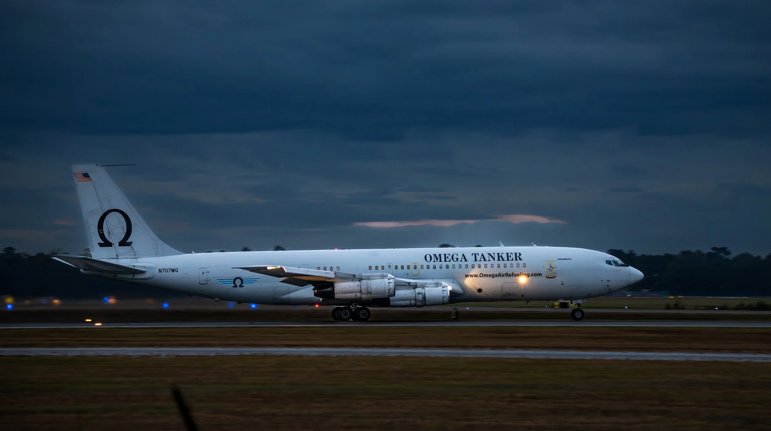 A large white airplane on a runway during dusk, with the words 'OMEGA TANKER' and the website 'www.OmegaAirRefueling.com' on the side.