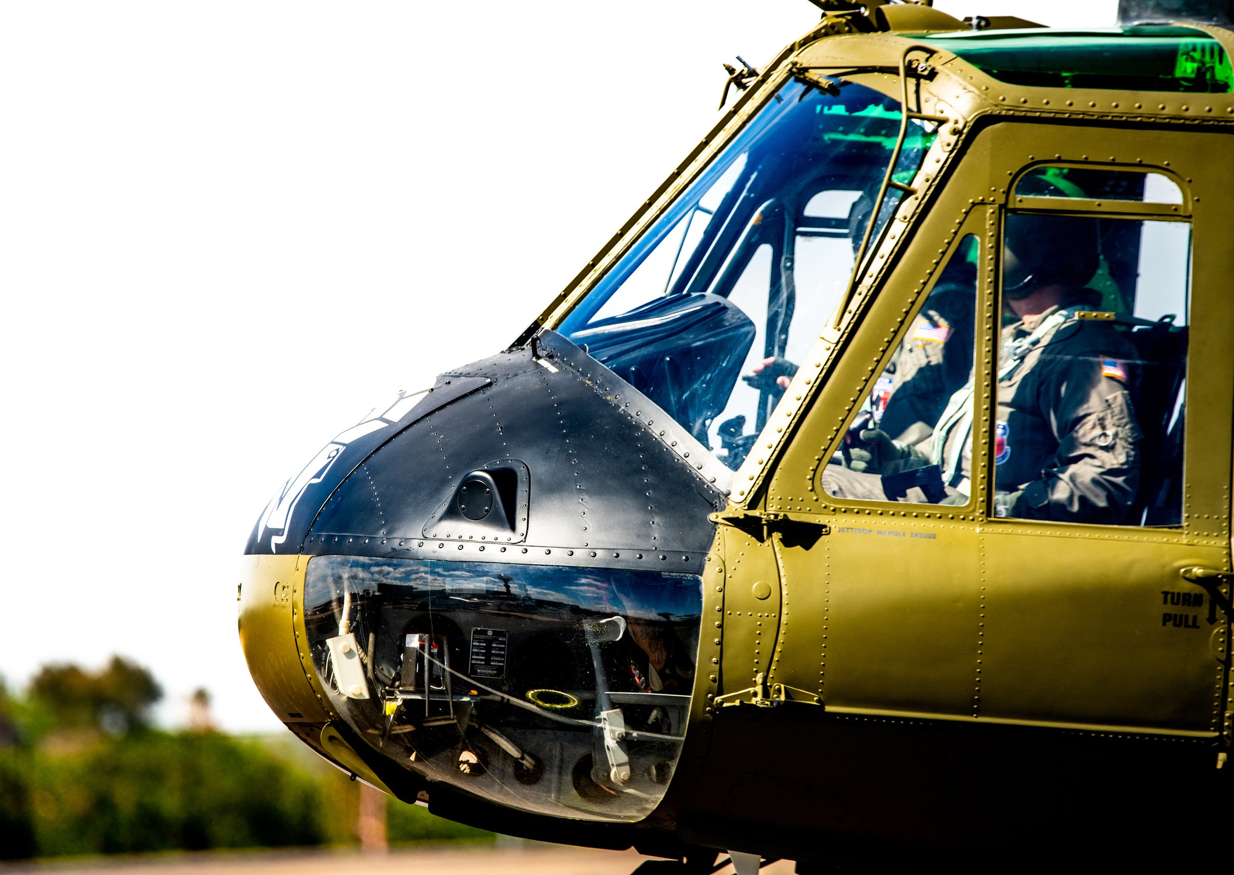 Close-up of a military helicopter cockpit with two pilots inside, wearing uniforms and helmets.