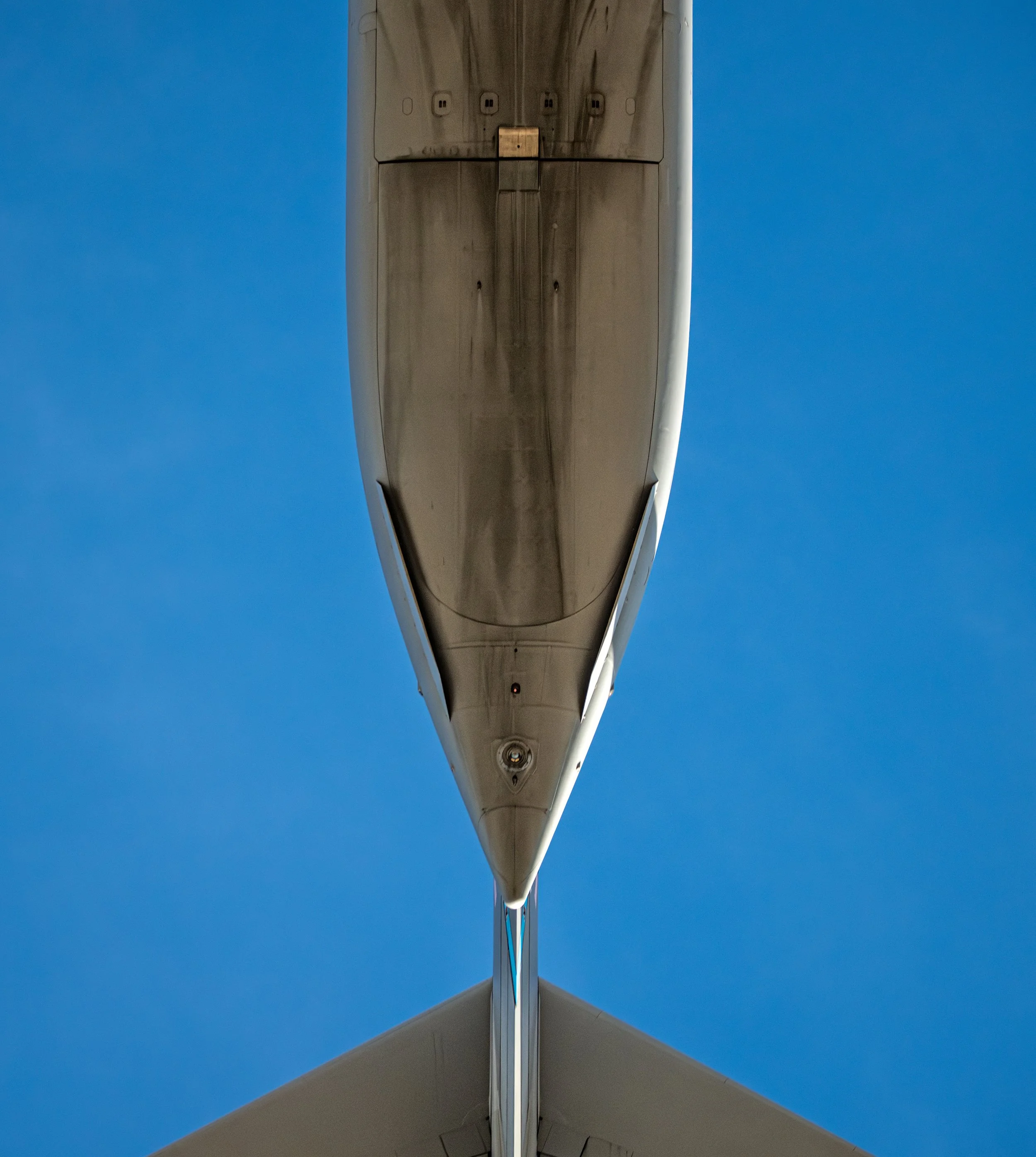 Close-up view of the underside of an airplane's wing and fuselage against a clear blue sky.