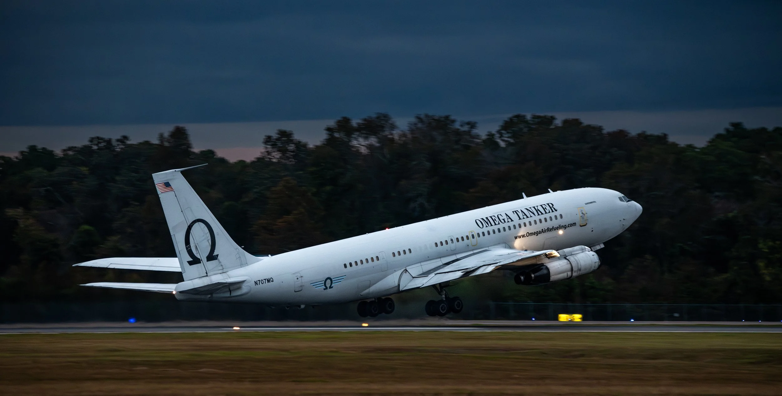 An airplane launching from a runway at dusk with dark clouds overhead, labeled 'Omega Tanker'.