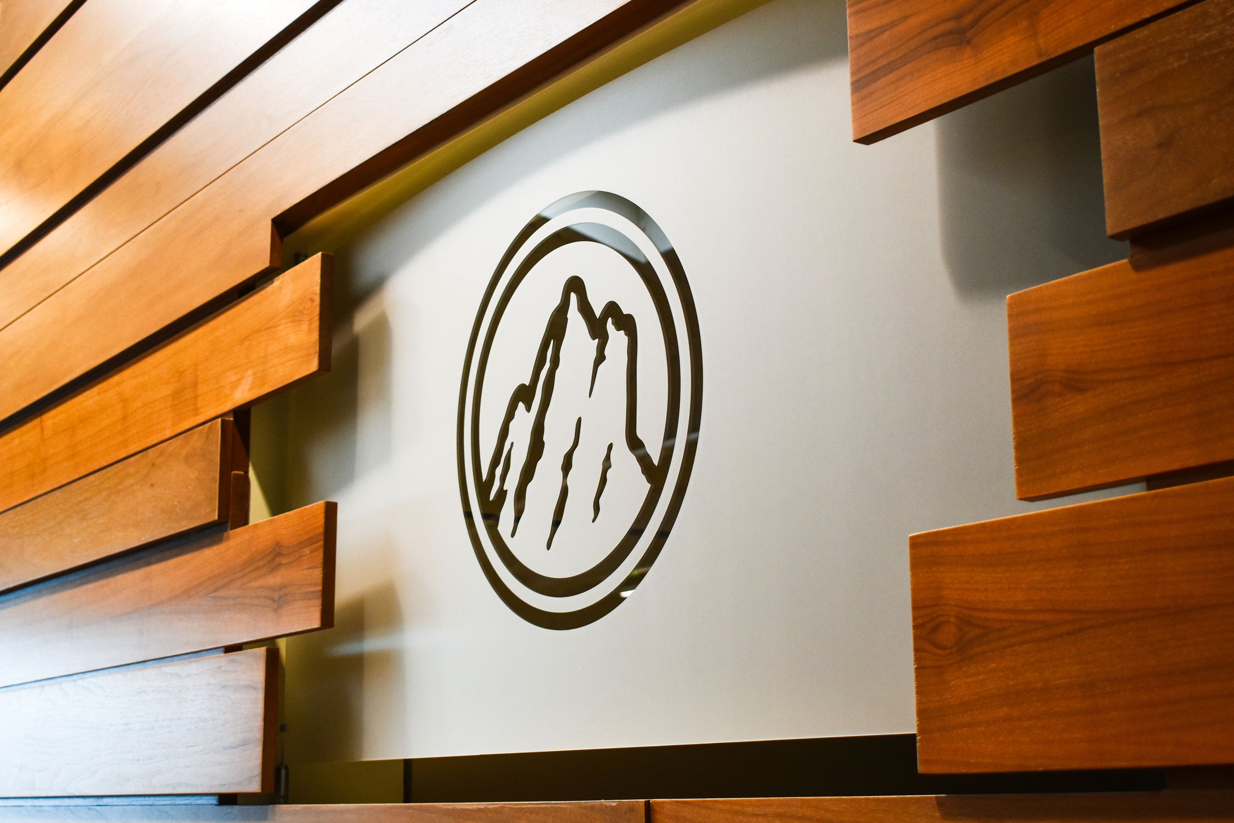 Wood panel wall with a white sign featuring a black circle and a mountain outline in the center.