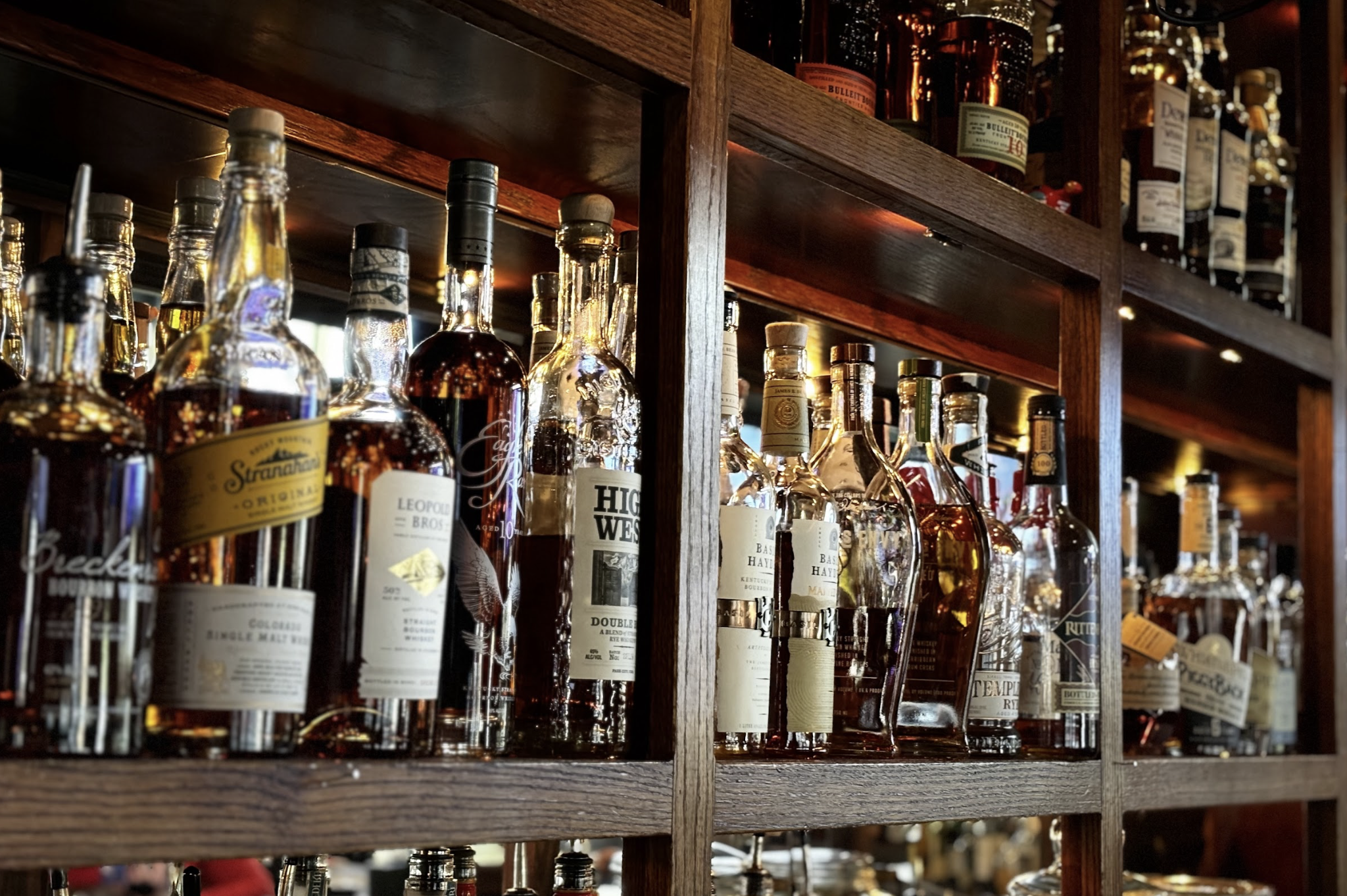A wooden shelf filled with various bottles of whiskey and liquor behind a bar.