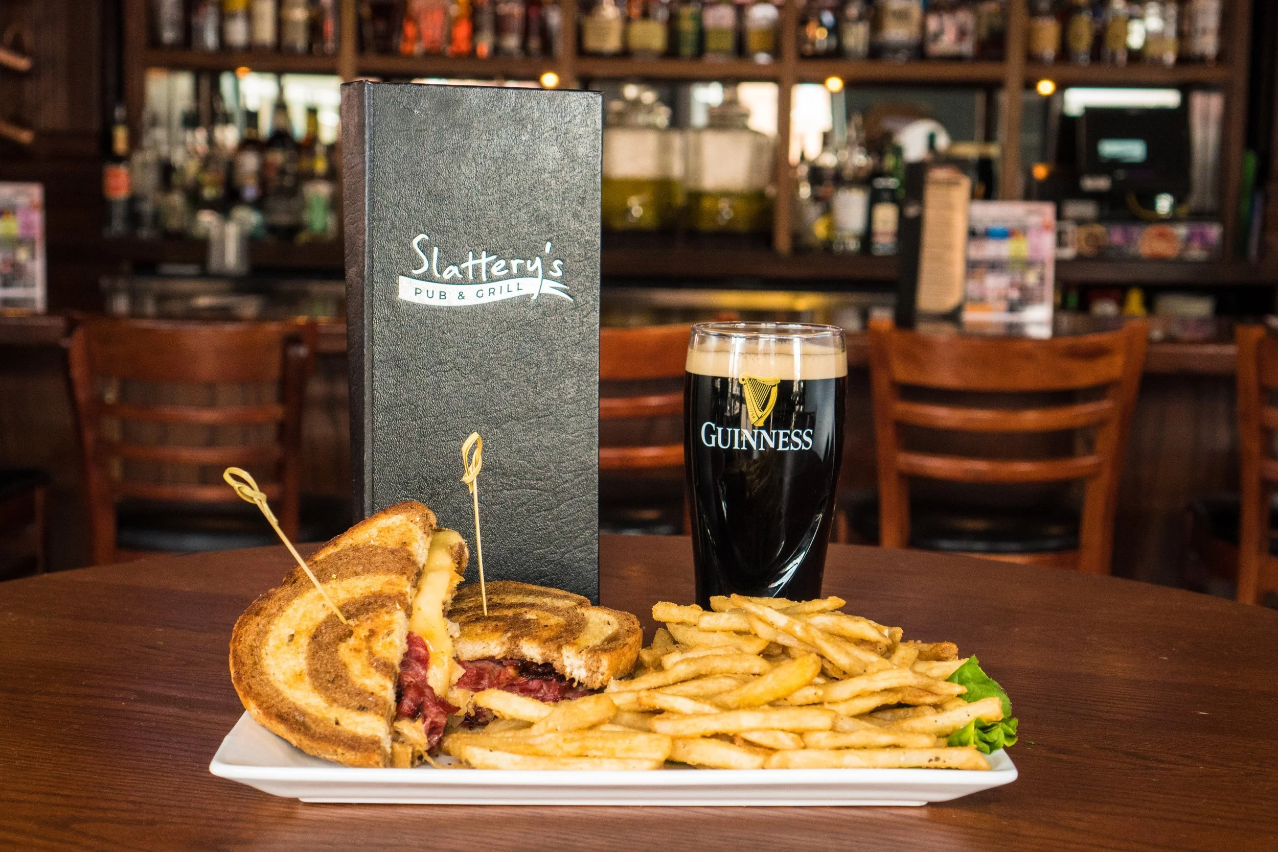 A plate with a toasted sandwich, French fries, a glass of Guinness beer, and a menu at a pub named Slattery's Pub & Grill in a restaurant setting.