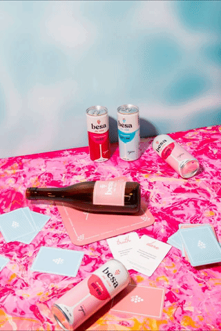 Various beverages and cards on a pink and blue floral tablecloth with a blue background, including a bottle of wine, cans of flavored water, and small blue boxes.