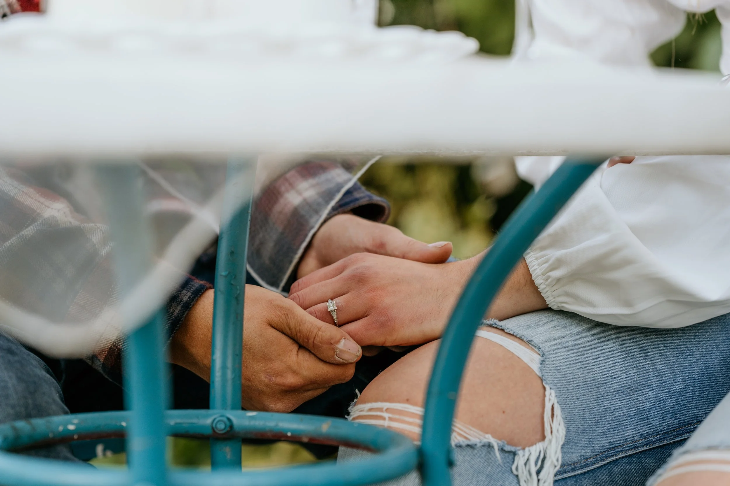 Man and woman with engagement ring holding hands under table