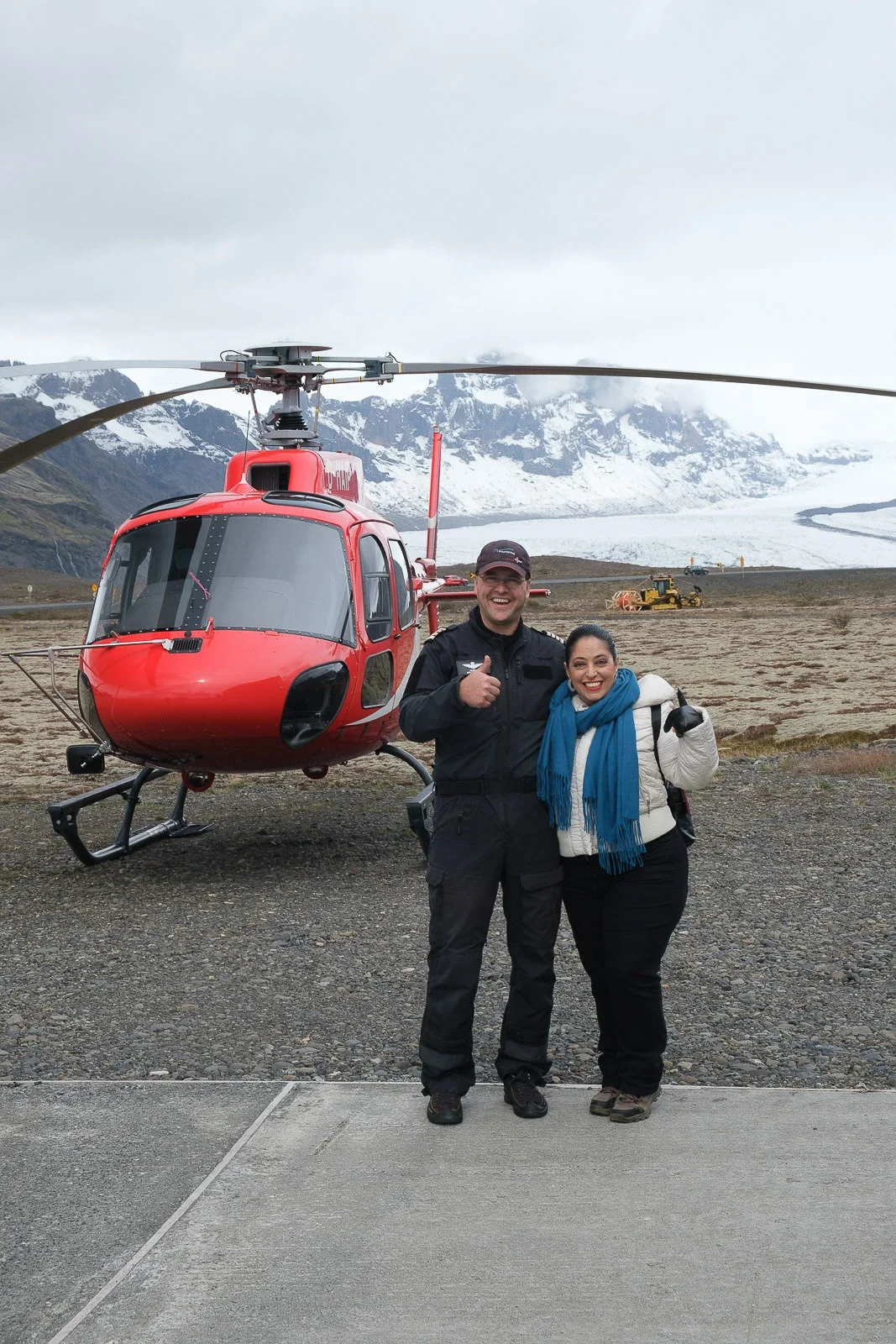 Tour guide and guest standing in front of a red helicopter used for accessible remote tours in Iceland