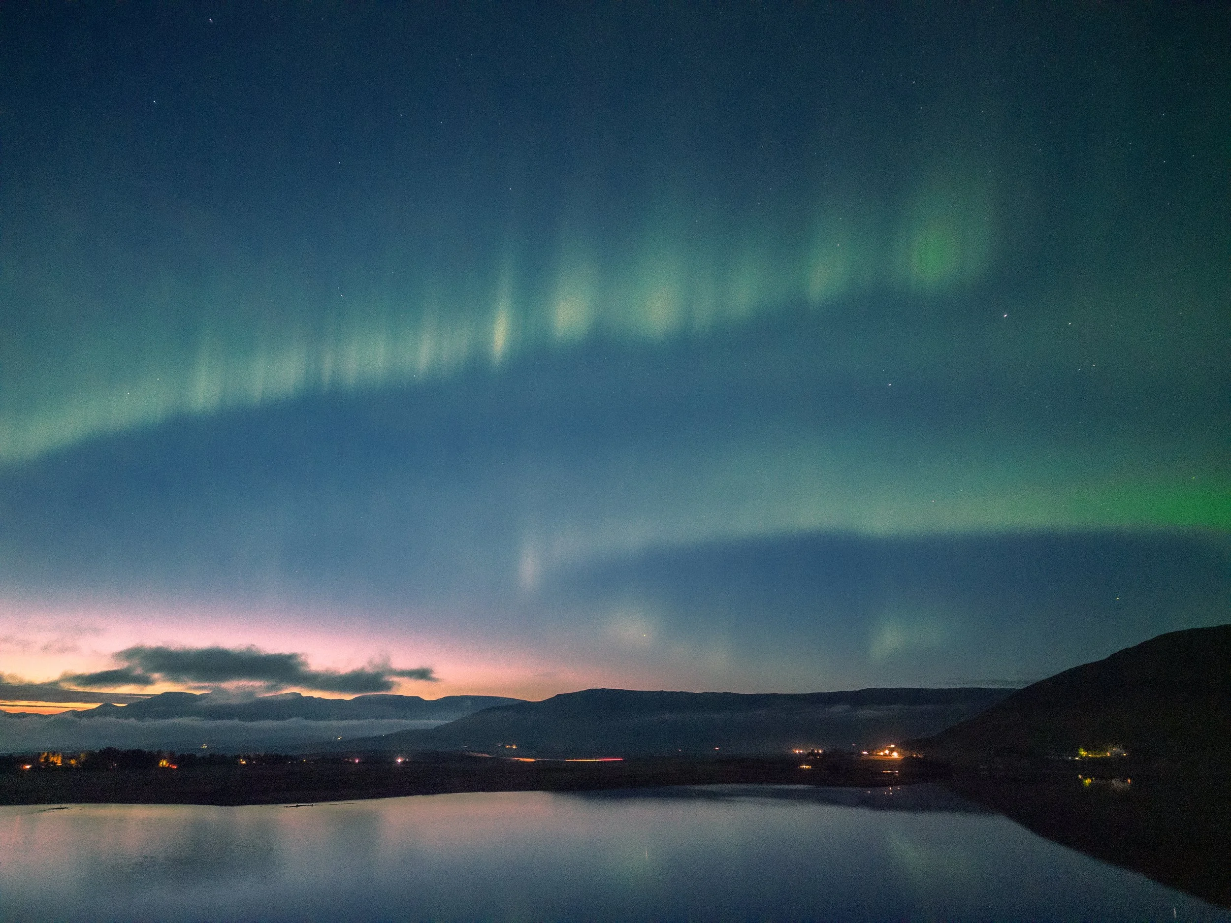 Night sky over mountains with visible northern lights (aurora borealis) and stars, in Iceland
