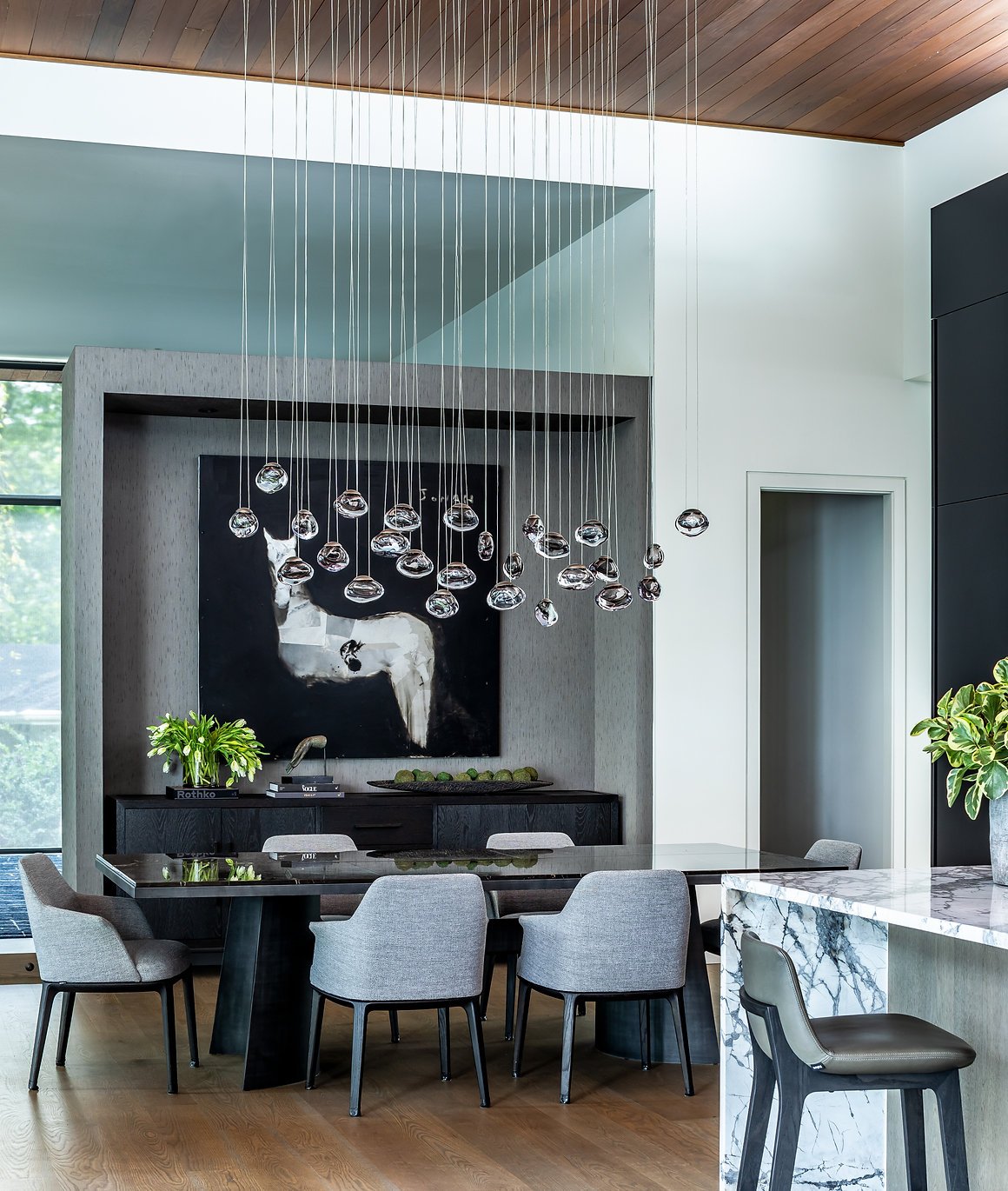 Modern dining room with a large Poliform table surrounded by gray chairs, abstract art on the wall, pendant light fixtures from Ochre, and wooden ceiling in Atlanta, GA.