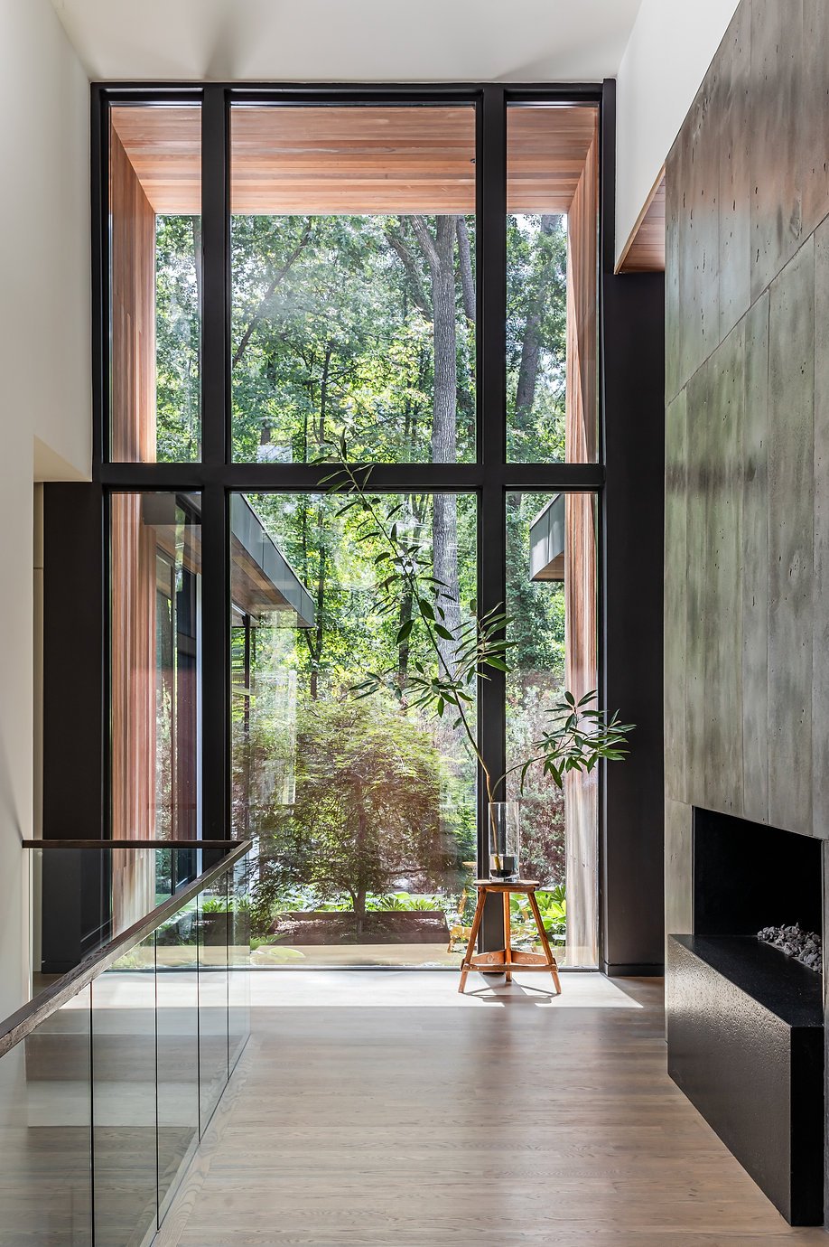 New construction of a modern interior with large window overlooking a lush garden, displaying a tall plant in a glass vase on a wooden stand and a sleek fireplace in Atlanta, GA.