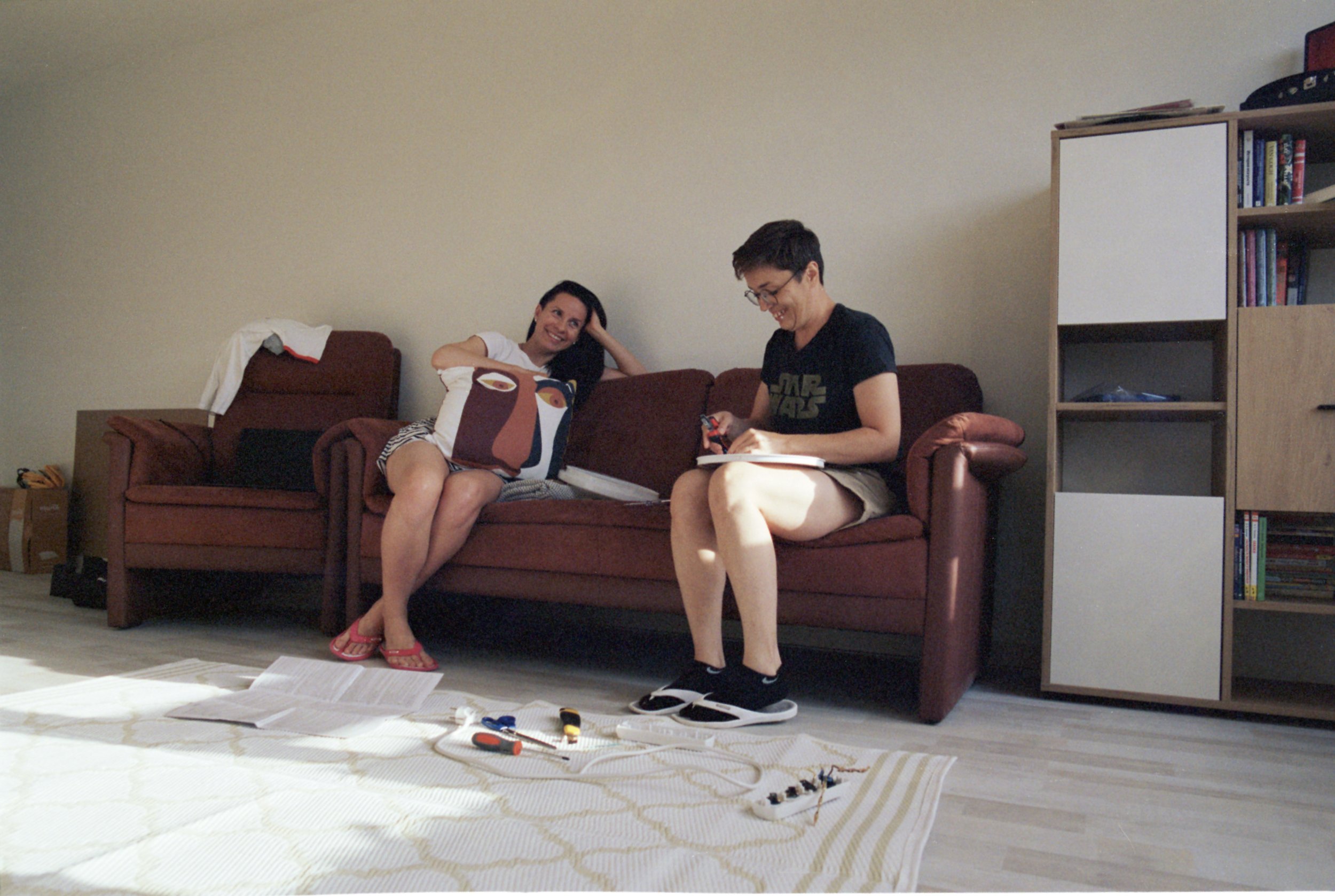Olga and Nataly on their couch, trying to fix up lighting in the apartment, laughing.
Empty walls in an apartment in a tiny town started to be filled with paint and decorations; inside space was happily welcoming second-hand furniture, donations, n