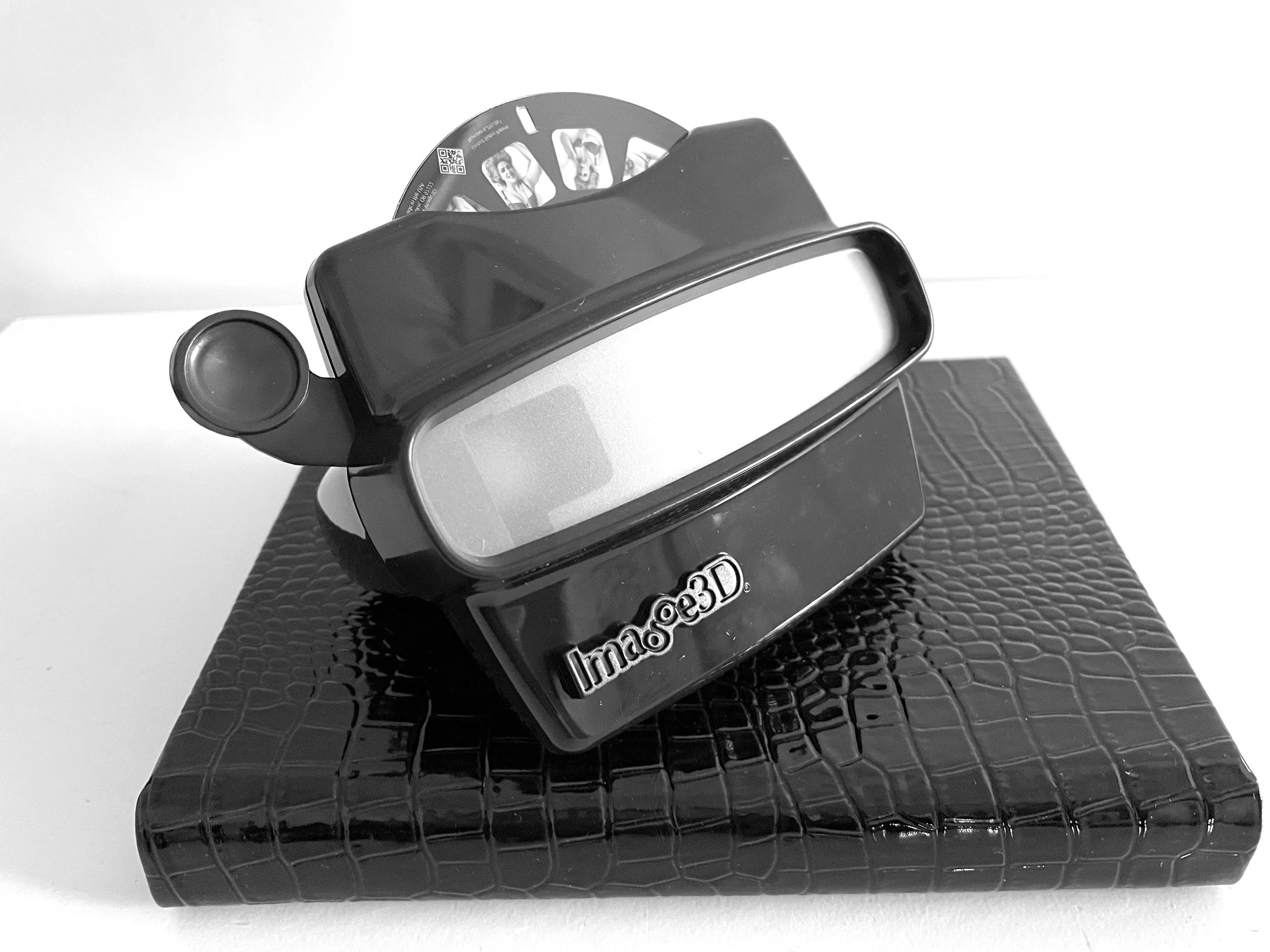A black and white photo of a 3D image projector device with the label 'Imagoo3D' placed on a textured black box.
