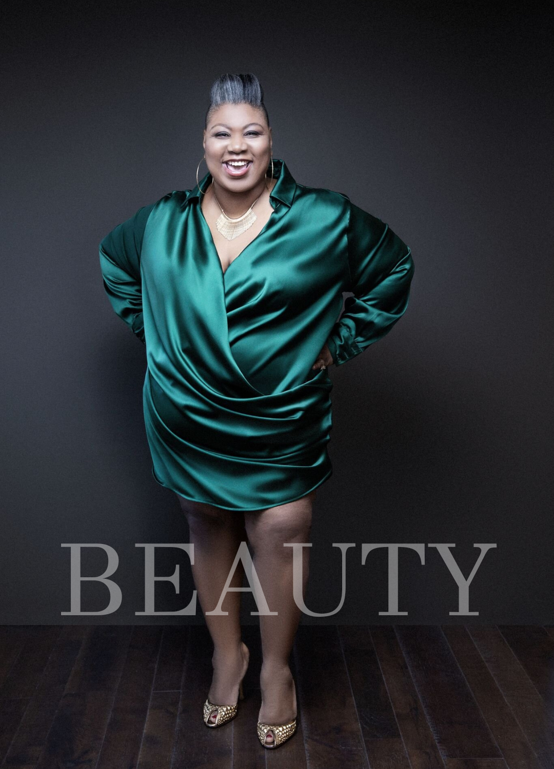 A confident woman wearing a shiny green satin dress, standing with hands on hips, smiling, with the word 'BEAUTY' overlaid at the bottom.