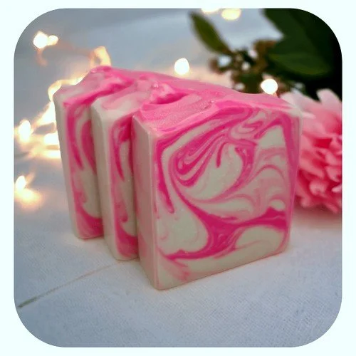 Handmade lychee peony soap with pink swirl design on white cloth with flowers and soft lights