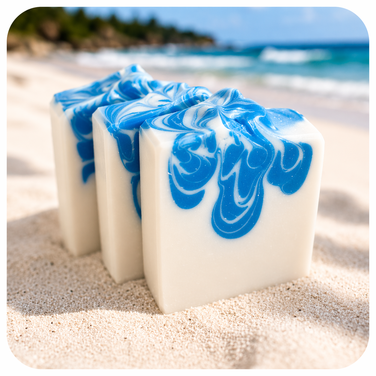 Handmade sea breeze soap with blue ocean swirl design on creamy white base styled on sandy beach background