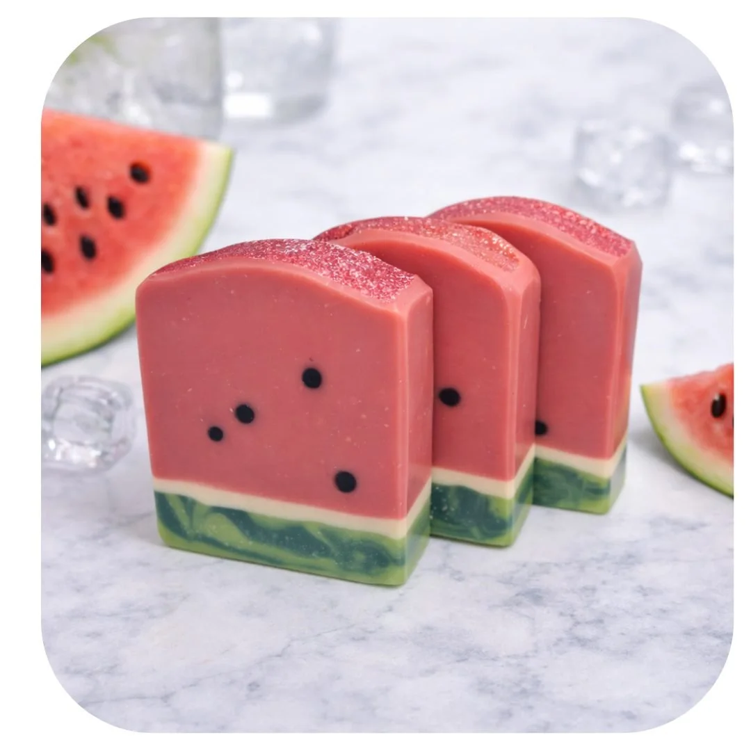 Handmade watermelon soap with pink and green layers and black seed details, styled with fresh watermelon slices.