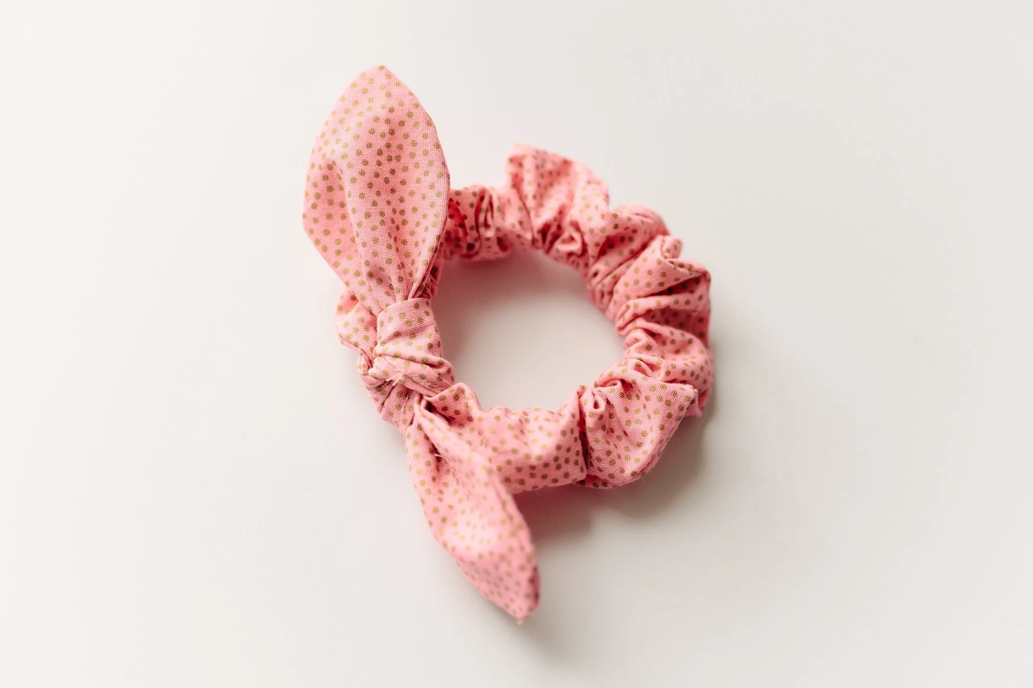 Pink fabric hair scrunchie with gold polka dots on a white background.