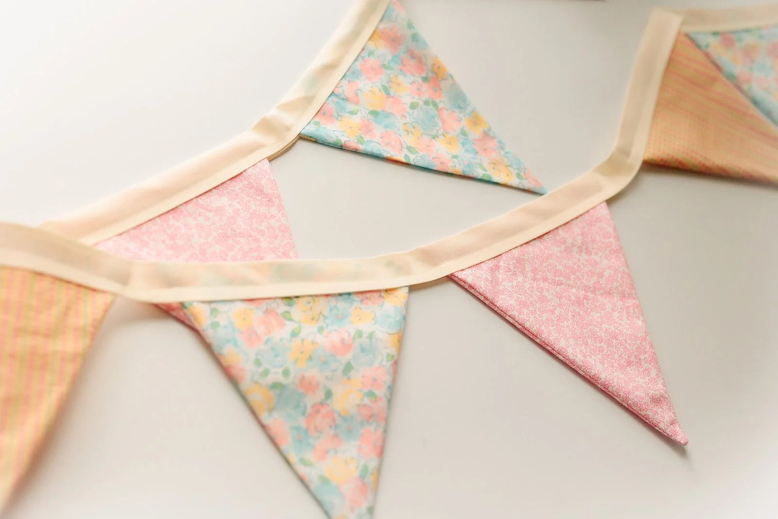 Close-up of a fabric bunting with pastel-colored triangular flags featuring floral and checkered patterns, strung on a cream-colored ribbon.