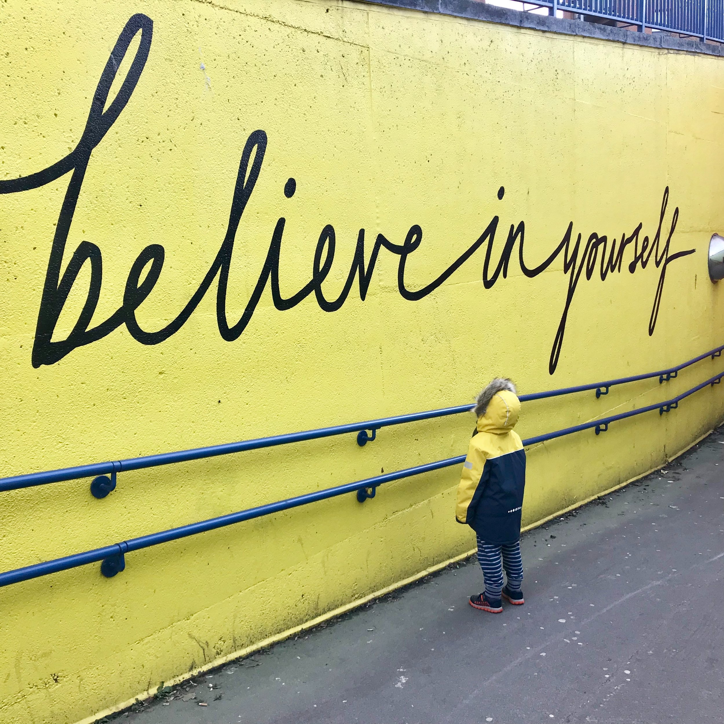 a child looking up at a yellow wall that says believe in yourself