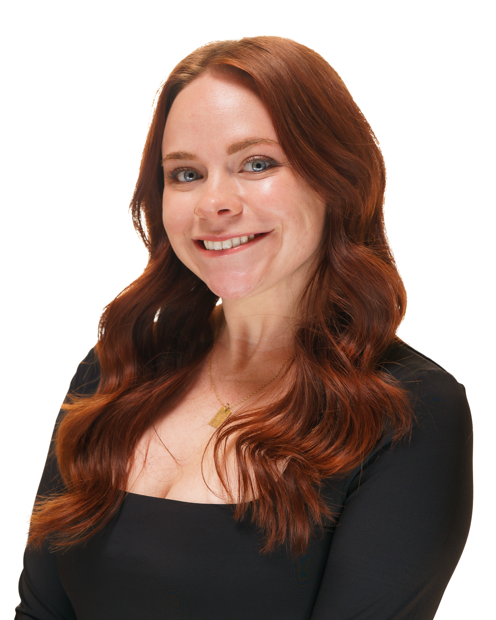 A woman with long red hair, blue eyes, and a nose ring, smiling while wearing a black top and a gold necklace.