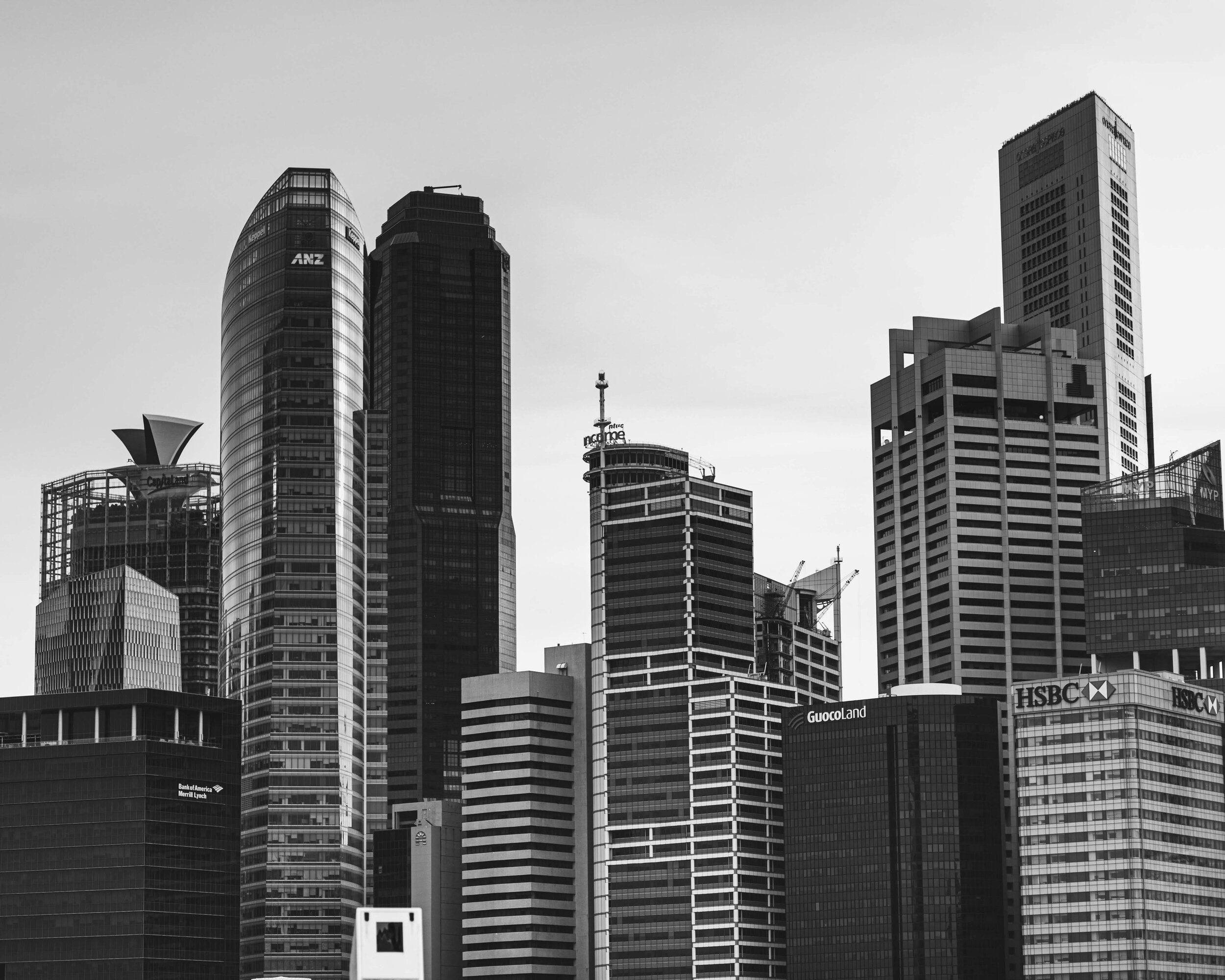 Black and white photo of a modern city skyline with several tall skyscrapers, including buildings labeled HSBC, GuocoLand, and ANZ.