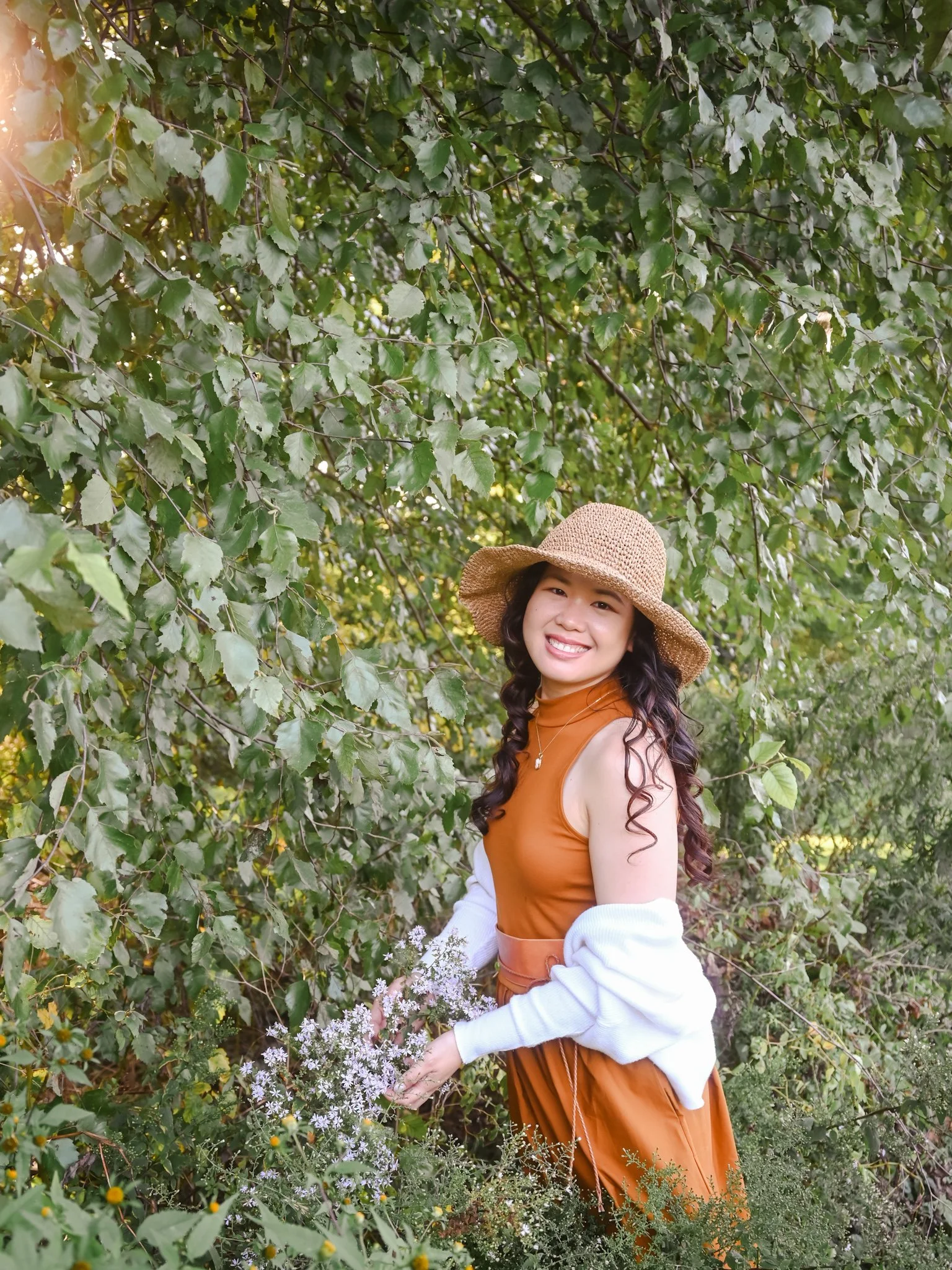 Cecile wearing a hat in the garden picking flowers while smiling at the camera