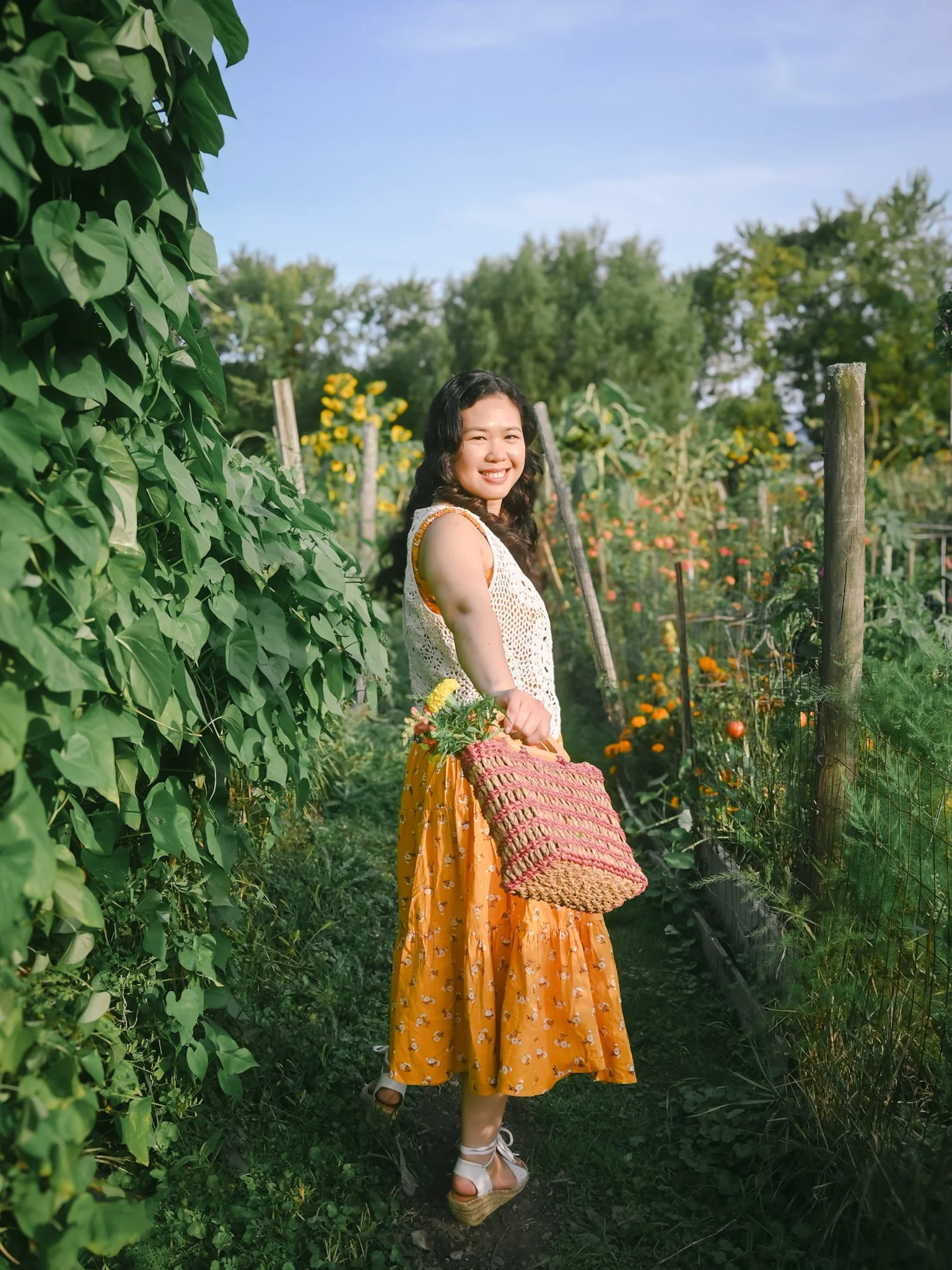 Cecille holding a bag of florals surrounded by rows of flowers in a fenced flower garden