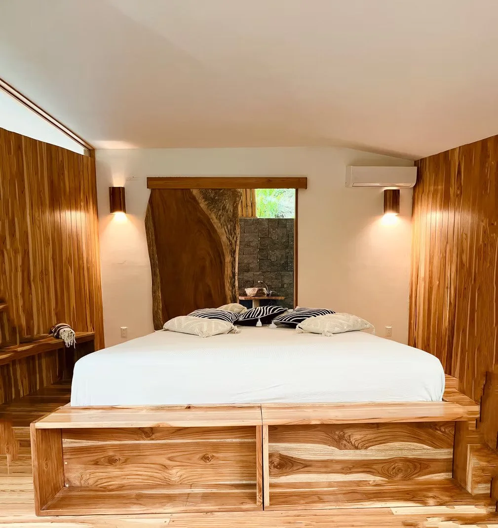A bedroom with a round bed, white bedding, wooden sliding doors, a stone accent wall, a beige chair, and a round woven rug.