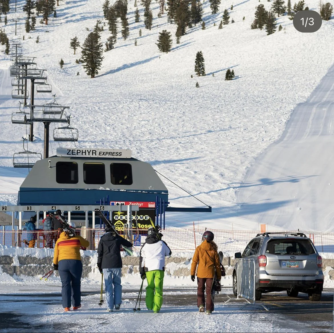 Skiers in winter clothing walking towards a ski lift at a snowy mountain ski resort.