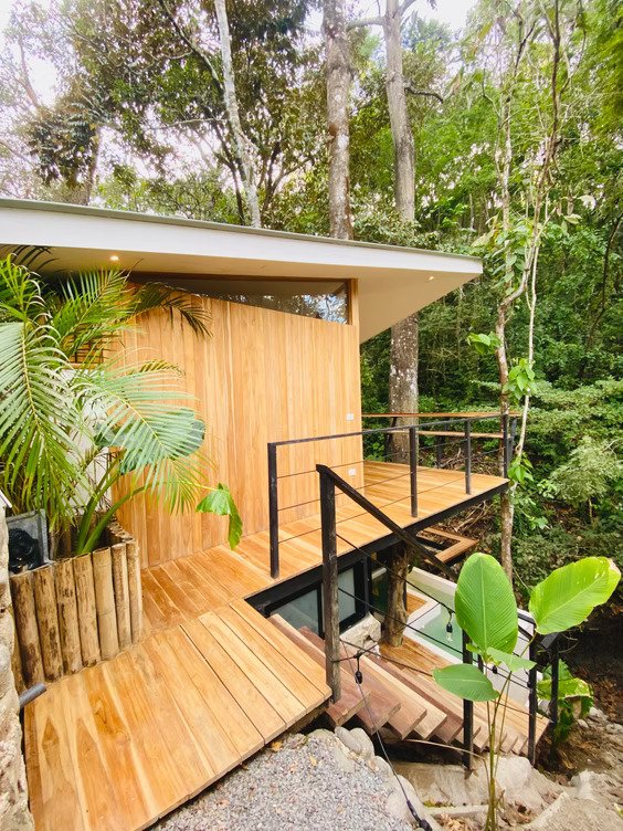 Woman relaxing in a small outdoor pool with a waterfall feature, surrounded by a potted plant and gravel
