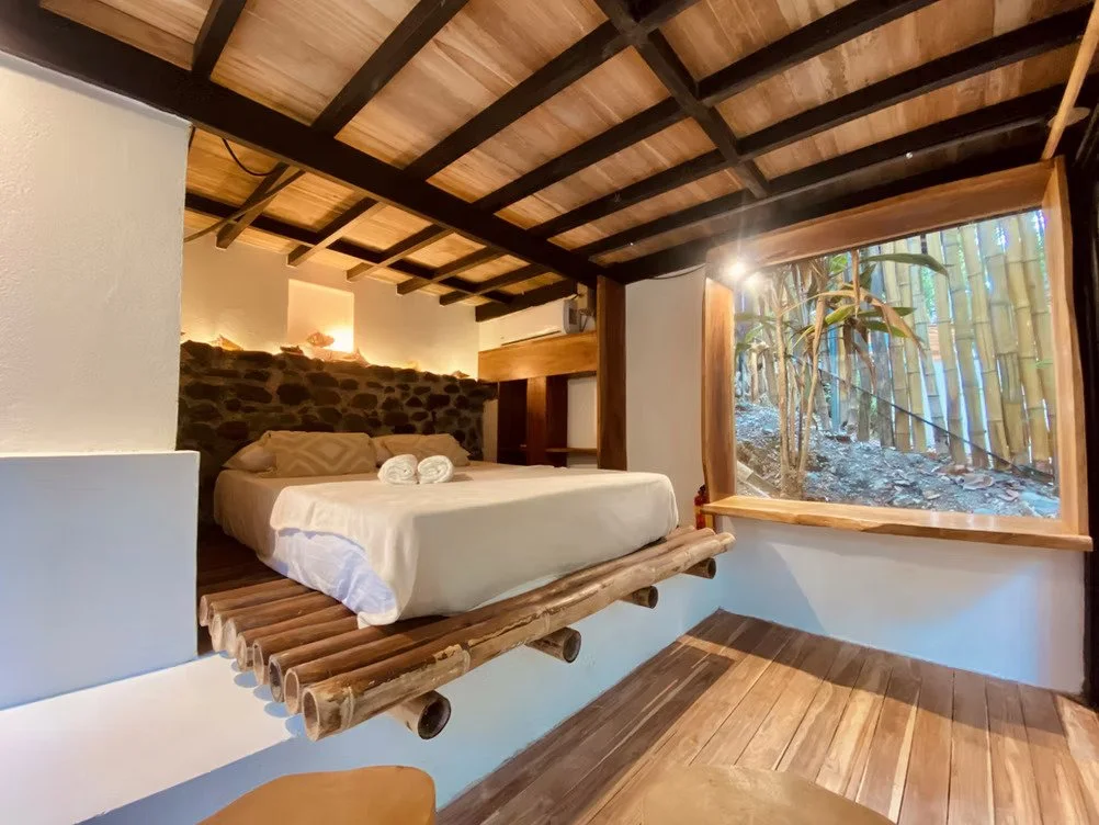 A bedroom with a round bed, white bedding, wooden sliding doors, a stone accent wall, a beige chair, and a round woven rug.