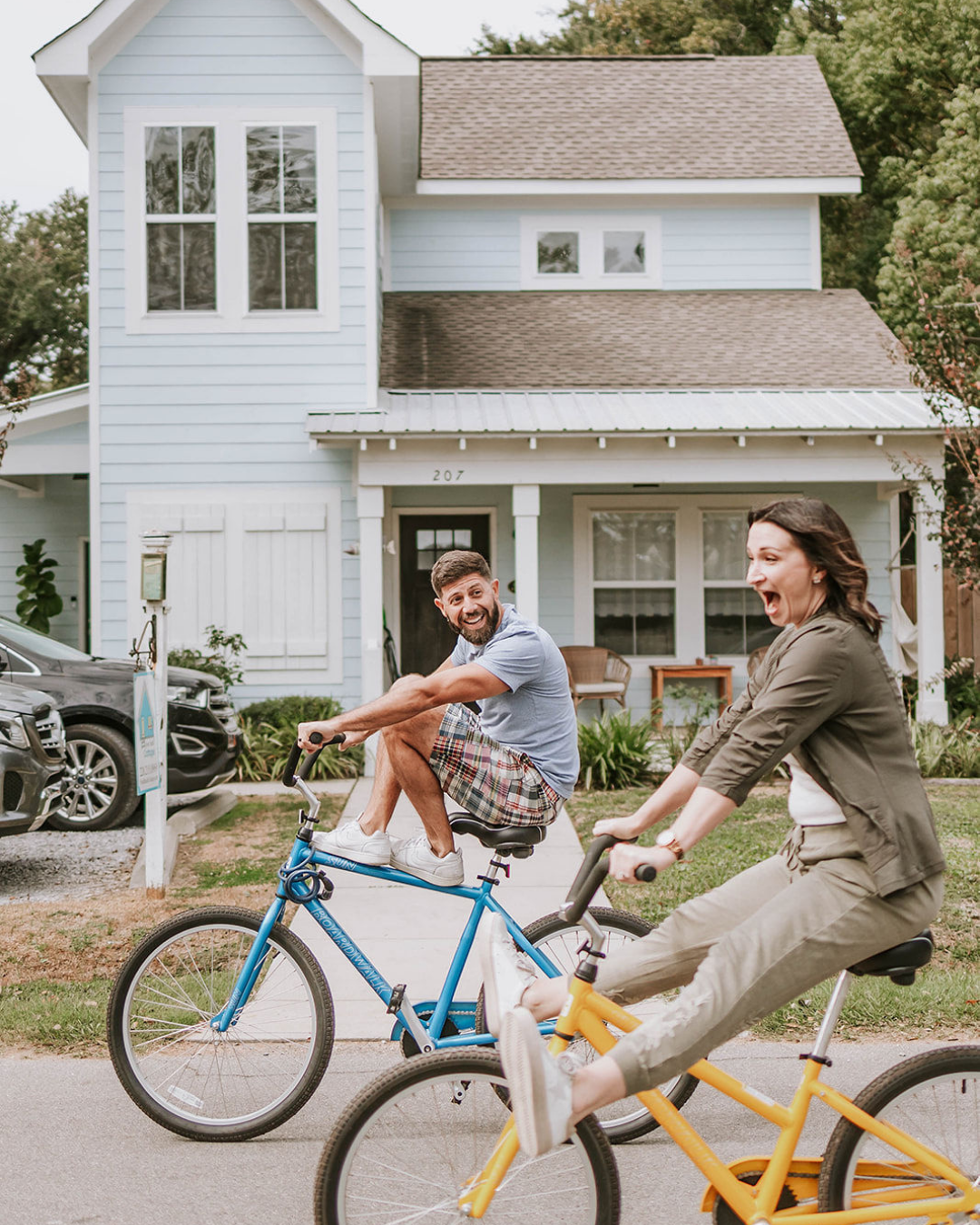 Lifestyle photography created for a client brandTwo people riding bicycles, smiling and enjoying a sunny day in front of a light blue house with white trim.
