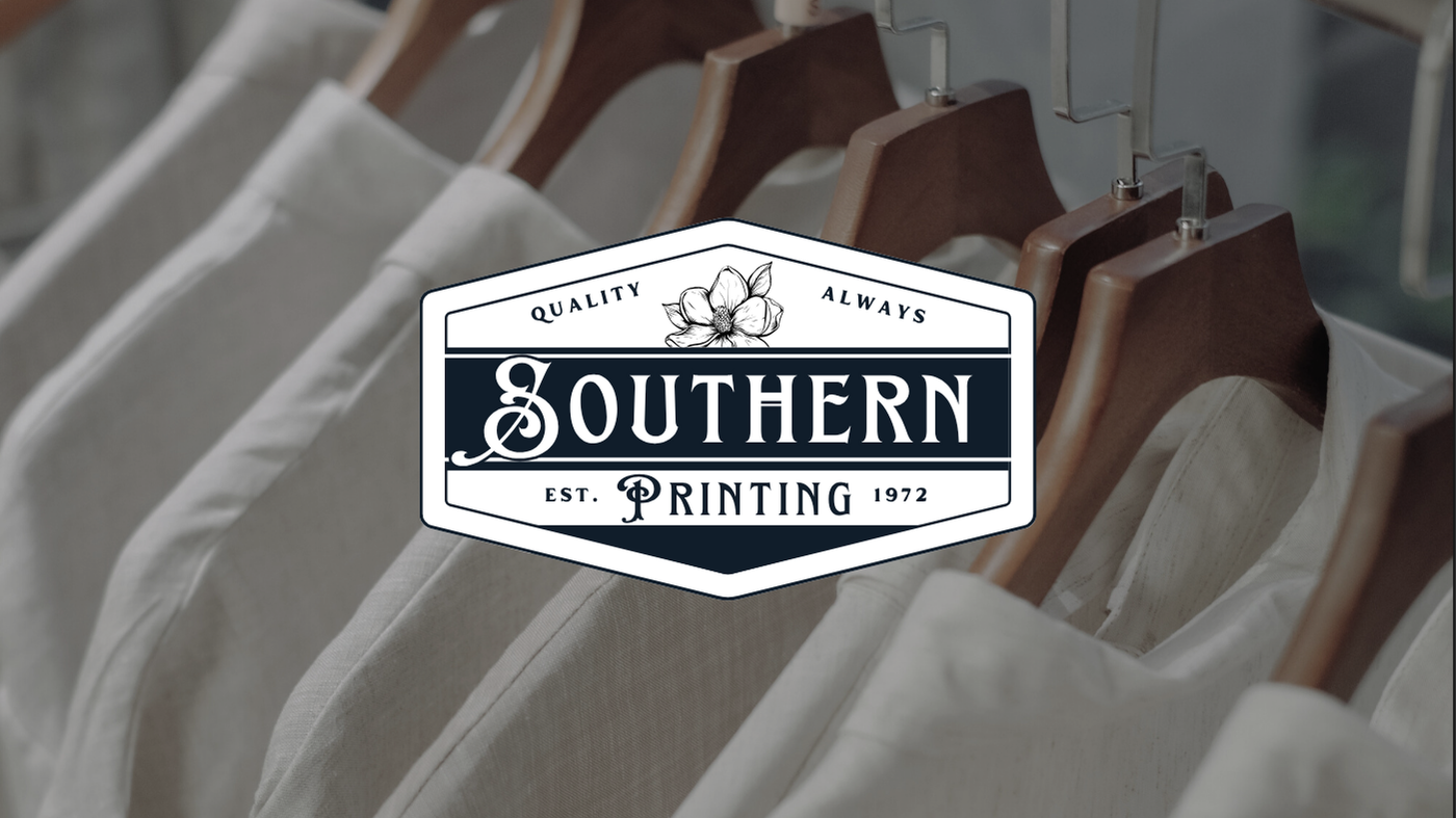 Clothing racks with white and beige shirts hanging on wooden hangers, with an overlaid logo reading 'Southern Printing' in black and white, established in 1972, featuring a flower illustration.