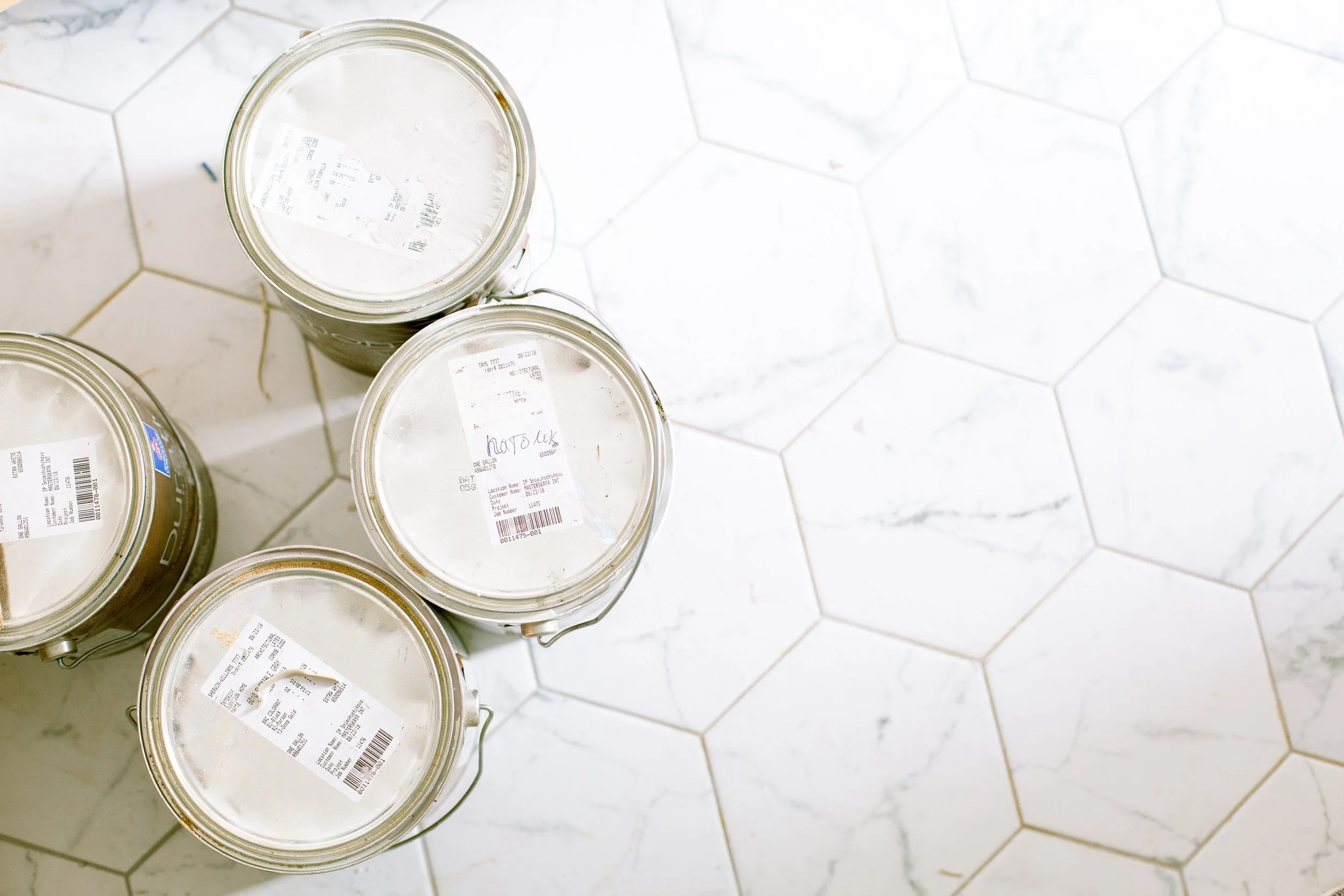 Five glass jars with labels on a white tiled floor.