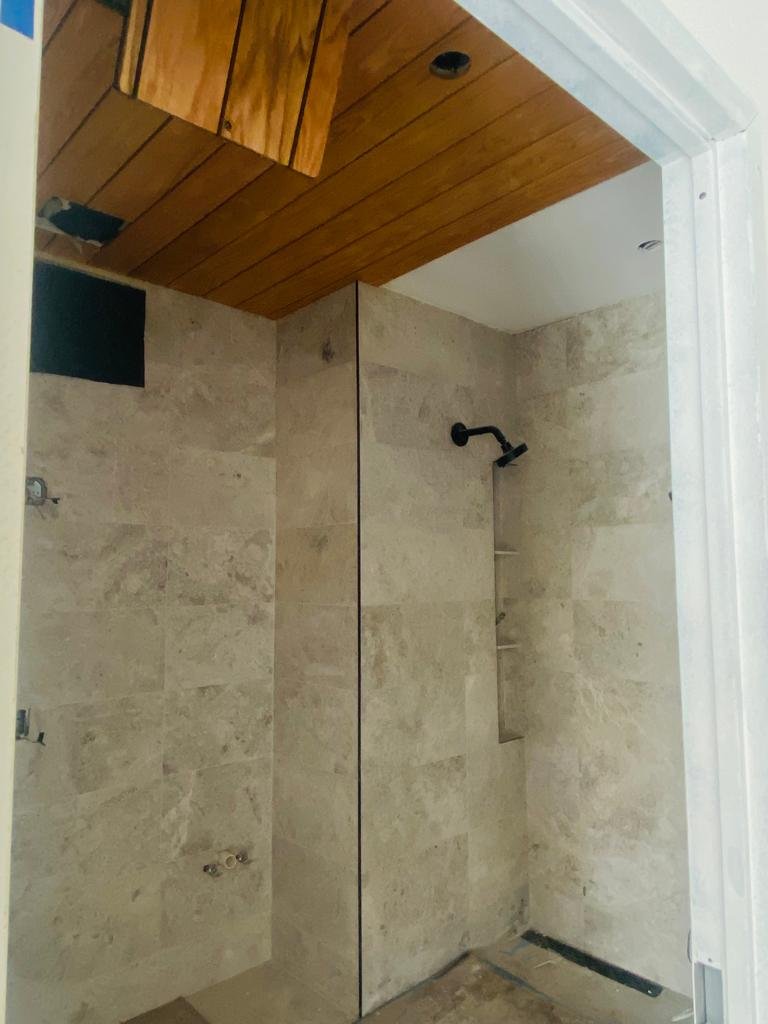 A bathroom shower area with beige tiled walls, a black showerhead, and a wood-paneled ceiling.