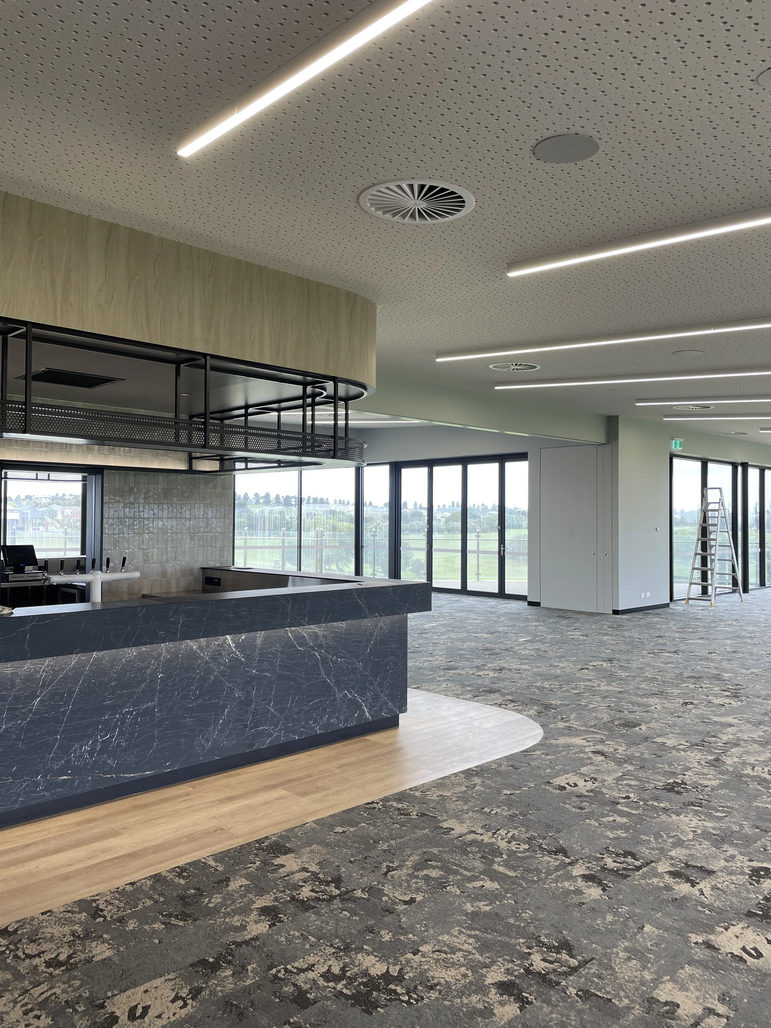 Modern interior space with large windows, a black marble reception desk, and a patterned carpet.