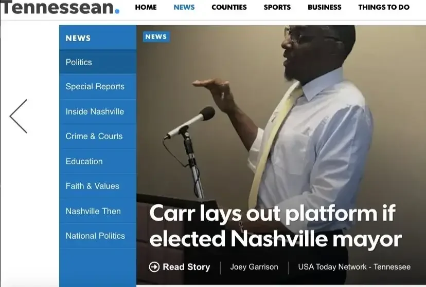 A man speaking at a podium with a microphone, wearing glasses, a white shirt, and a yellow tie, gesturing with one hand during a news presentation on the Tennesseean website about Carr outlining a platform if elected Nashville mayor.