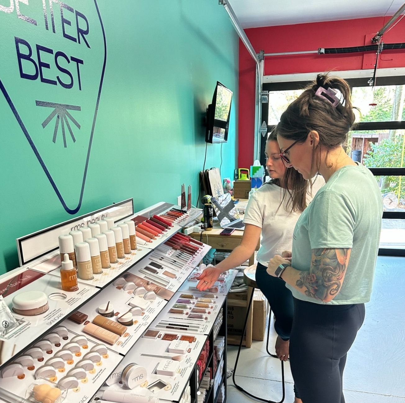 Two women shopping for makeup products inside a store with a turquoise wall and a large logo.